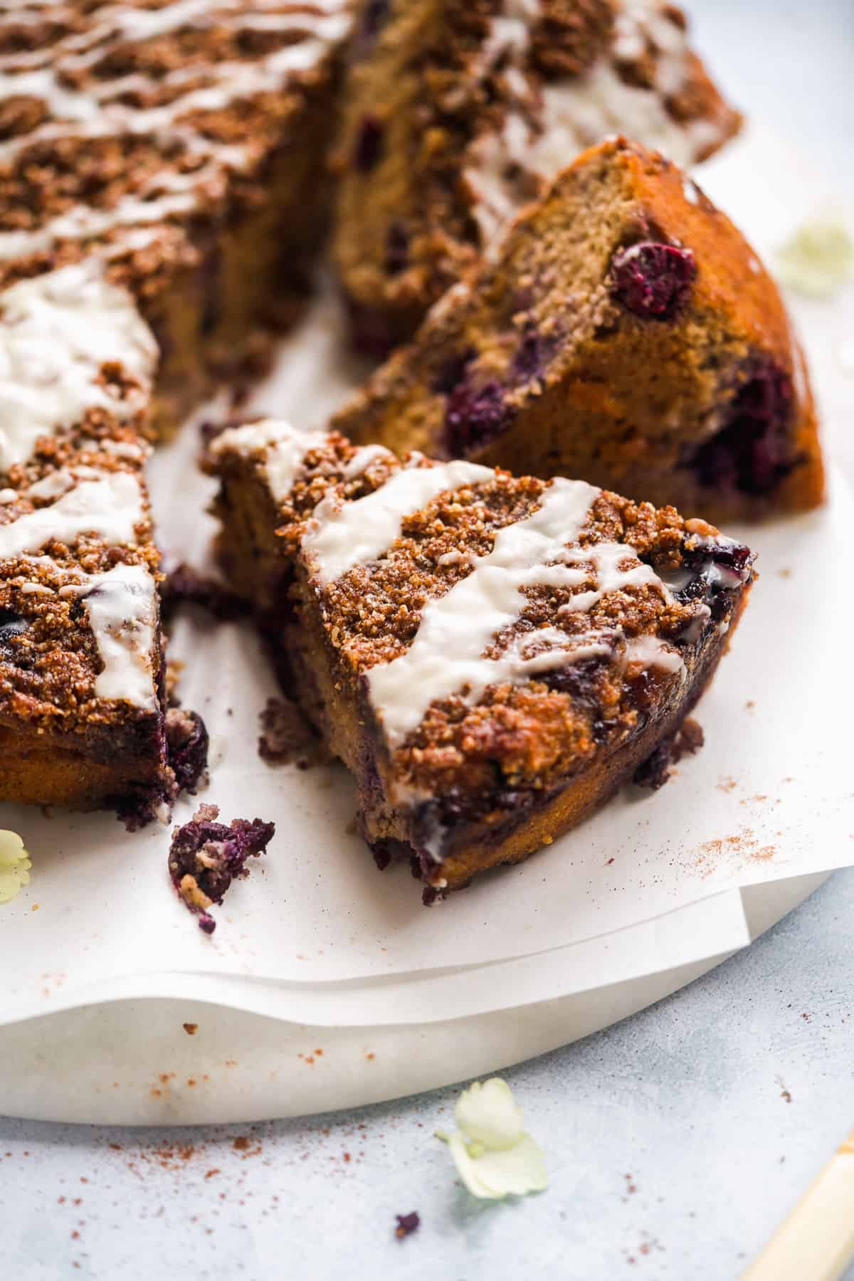 Coffee cake with blueberries and white glaze scattered on white parchment paper.