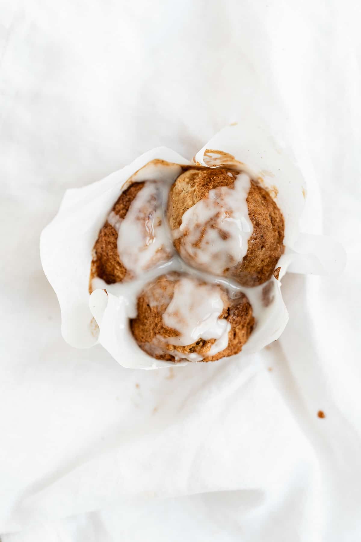 Single muffin with a white paper liner and white glaze dripping off the sides.