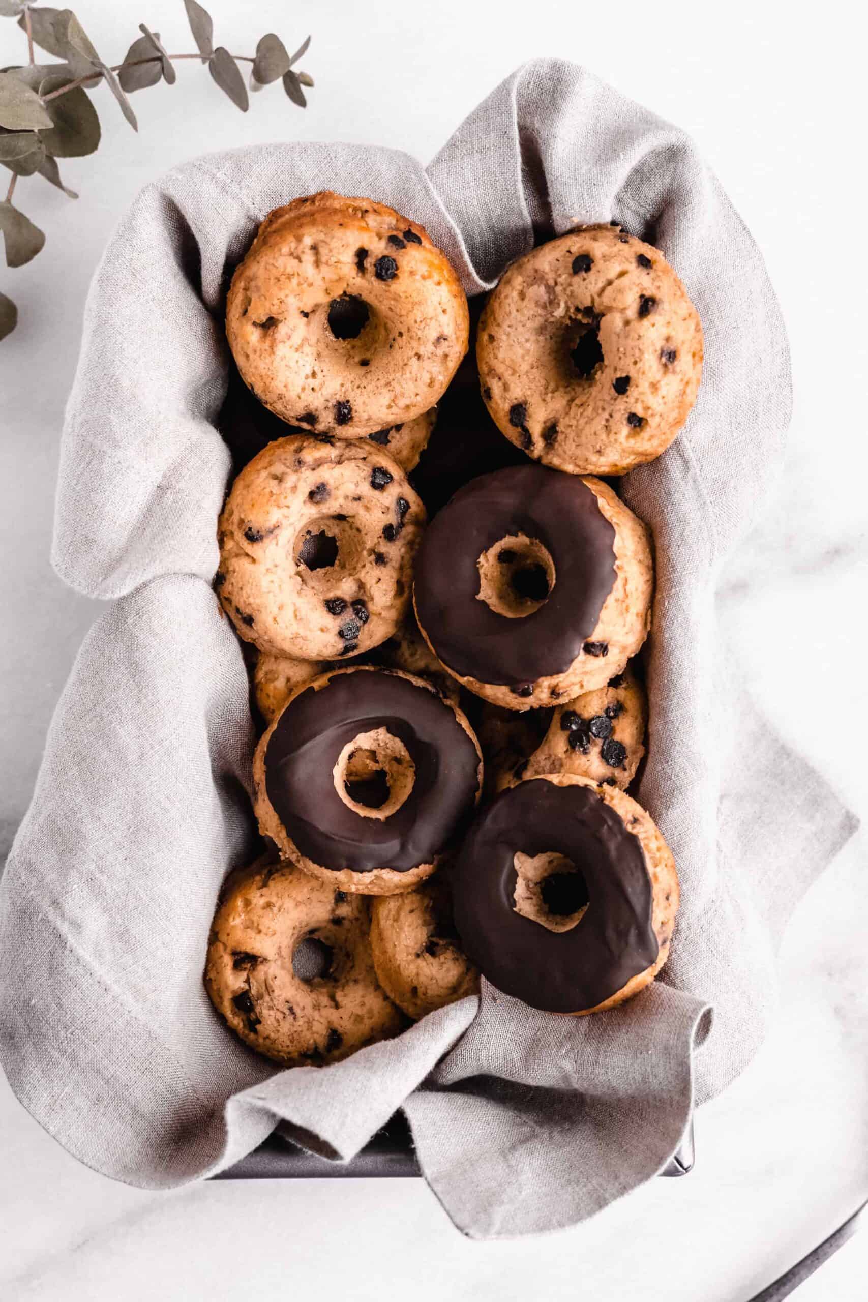 Pile of chocolate chip doughnuts in a basket with grey linen.