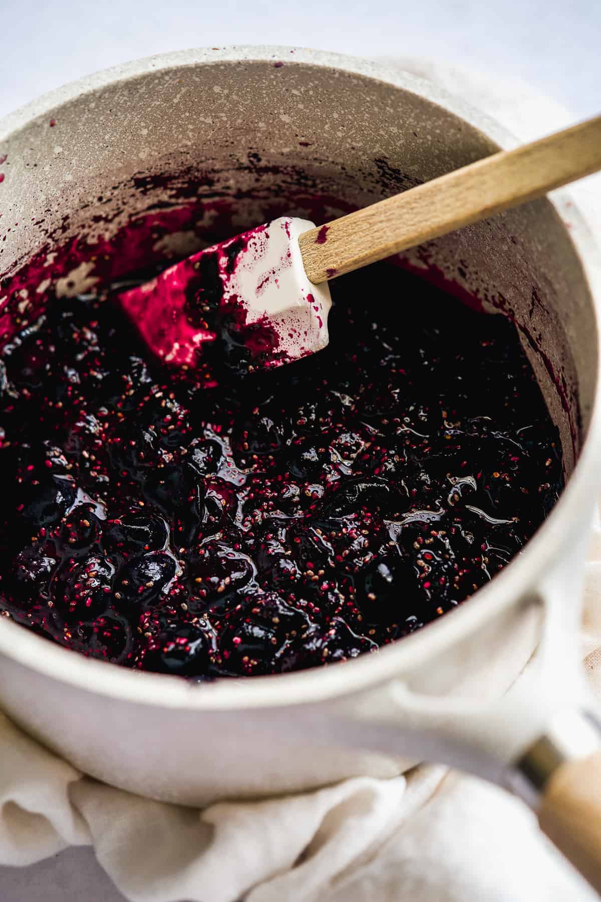 Spatula stirring a pot of cooking blueberries.