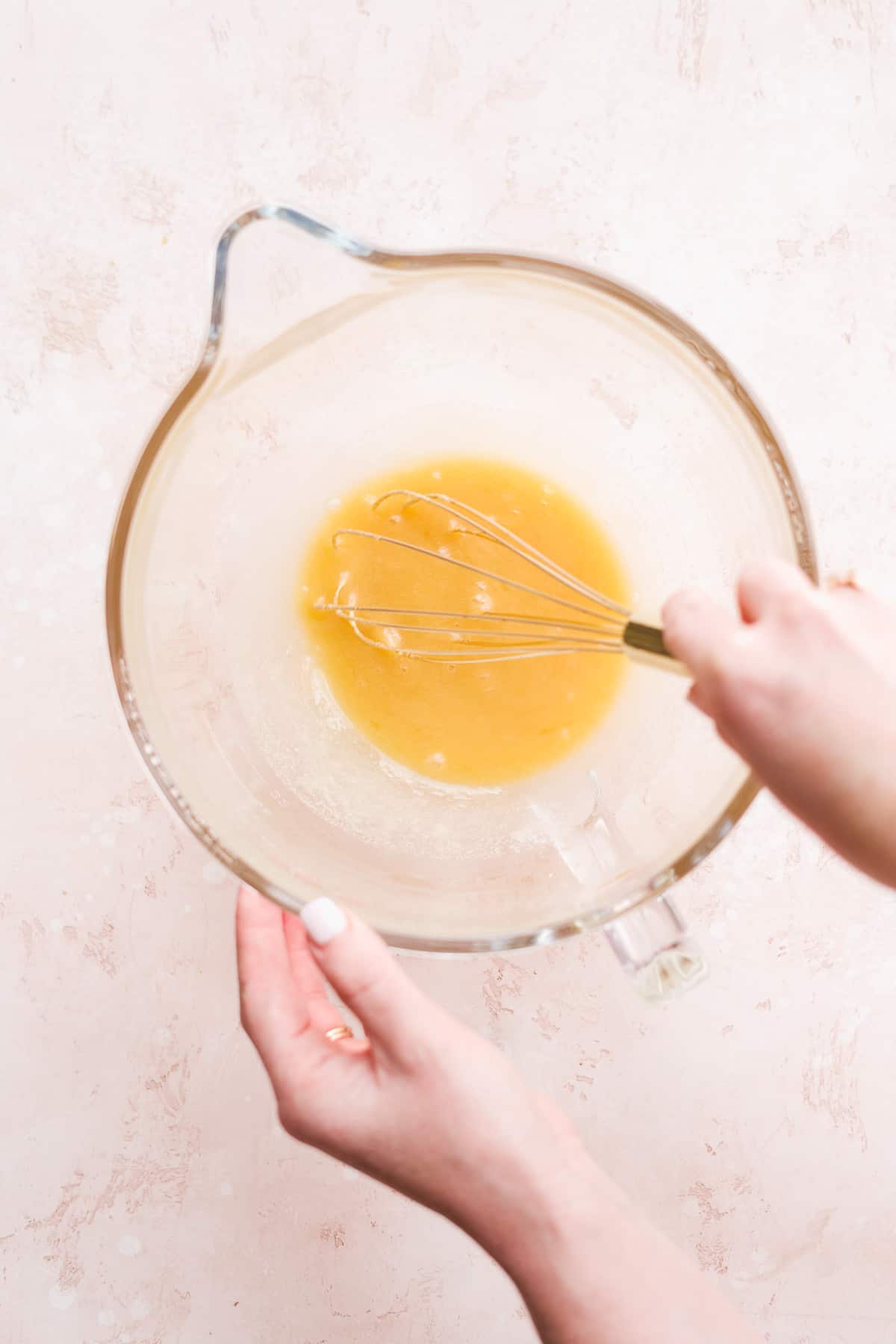 Hand whisking ingredients in glass bowl.