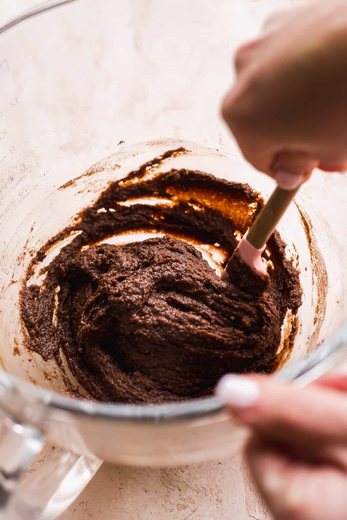 Person mixing chocolate doughnut batter in a glass bowl.