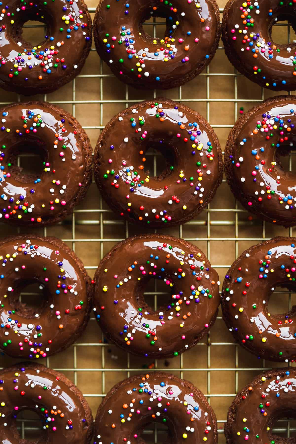 Chocolate doughnuts with sprinkles on a wired rack.