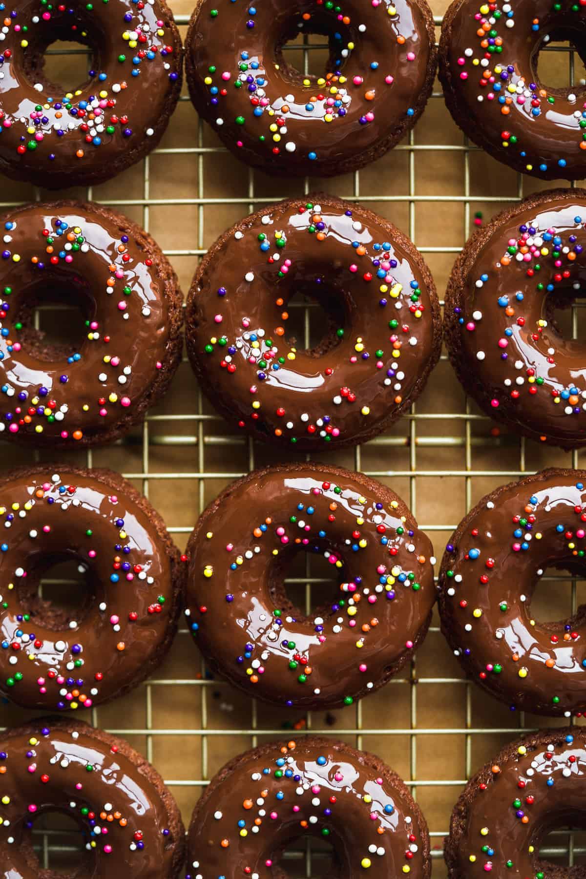 Chocolate doughnuts with sprinkles on a wired rack.