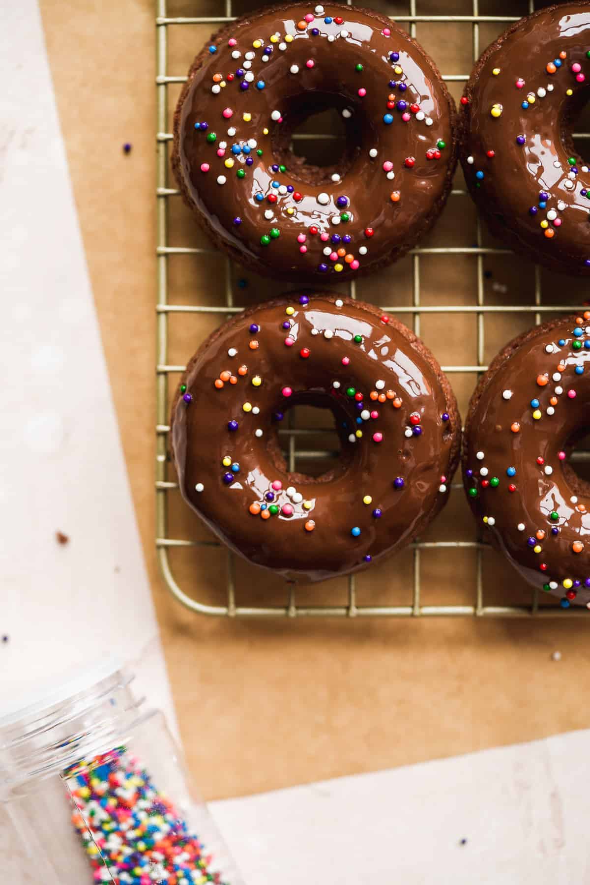 Up close shot of chocolate doughnut with sprinkles on wire rack.