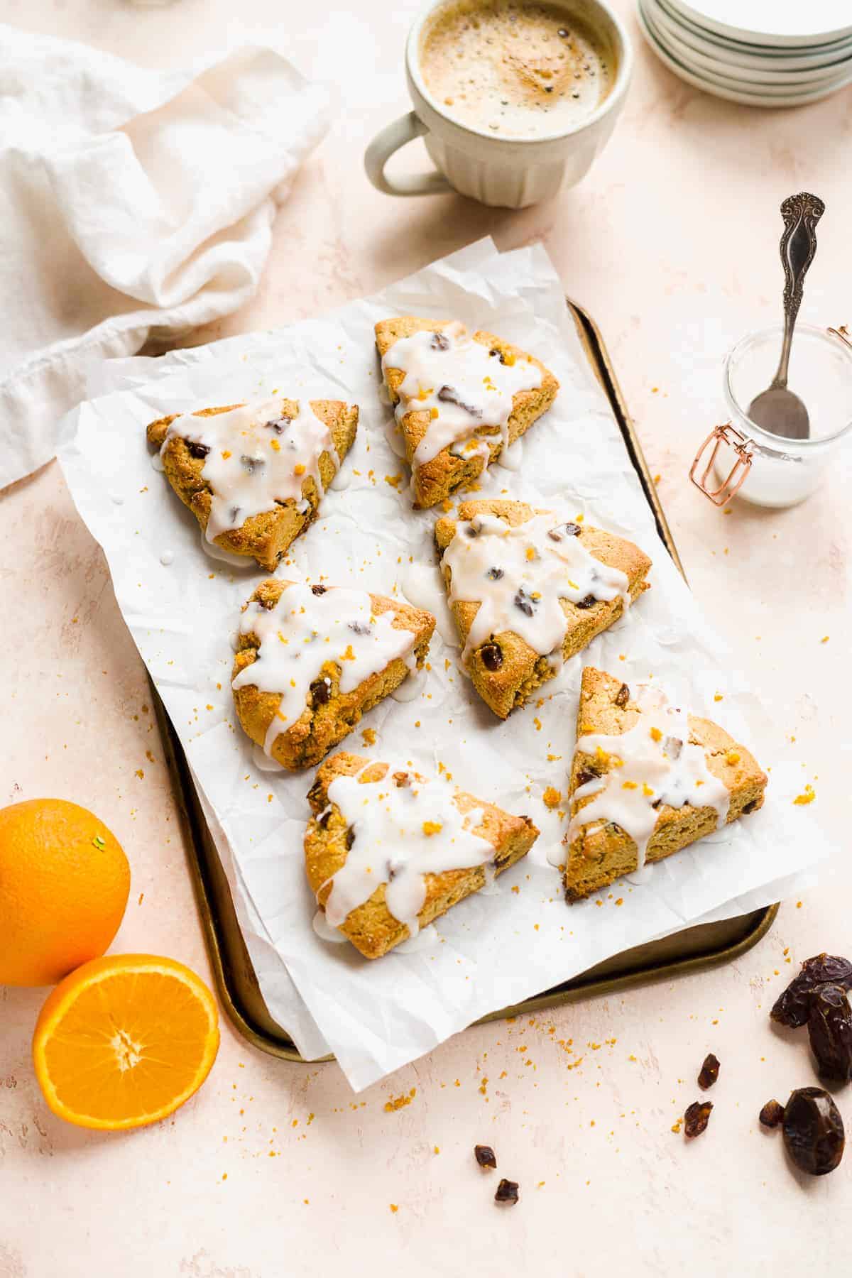 Triangular scones with glaze on parchment paper on top of a baking sheet with orange on the side.