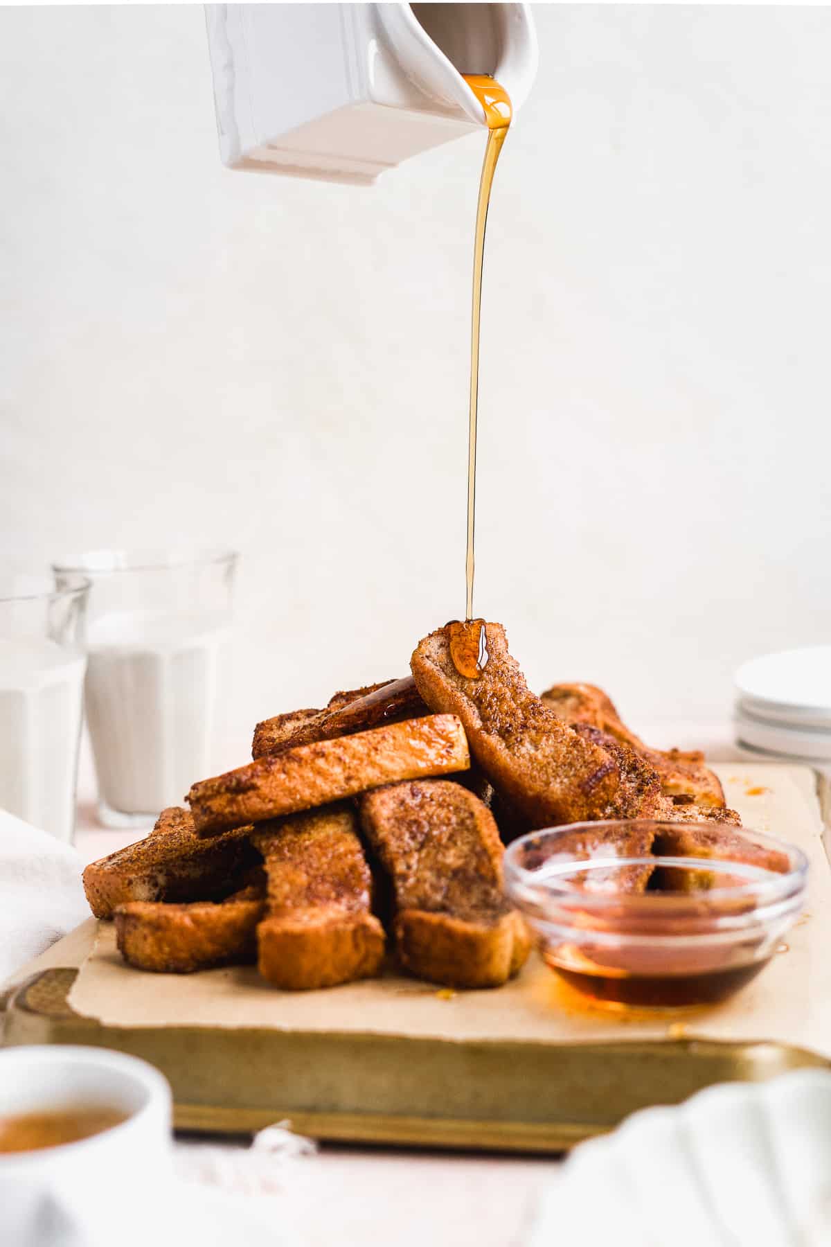 Maple syrup being poured on top of a pile of french toast sticks.