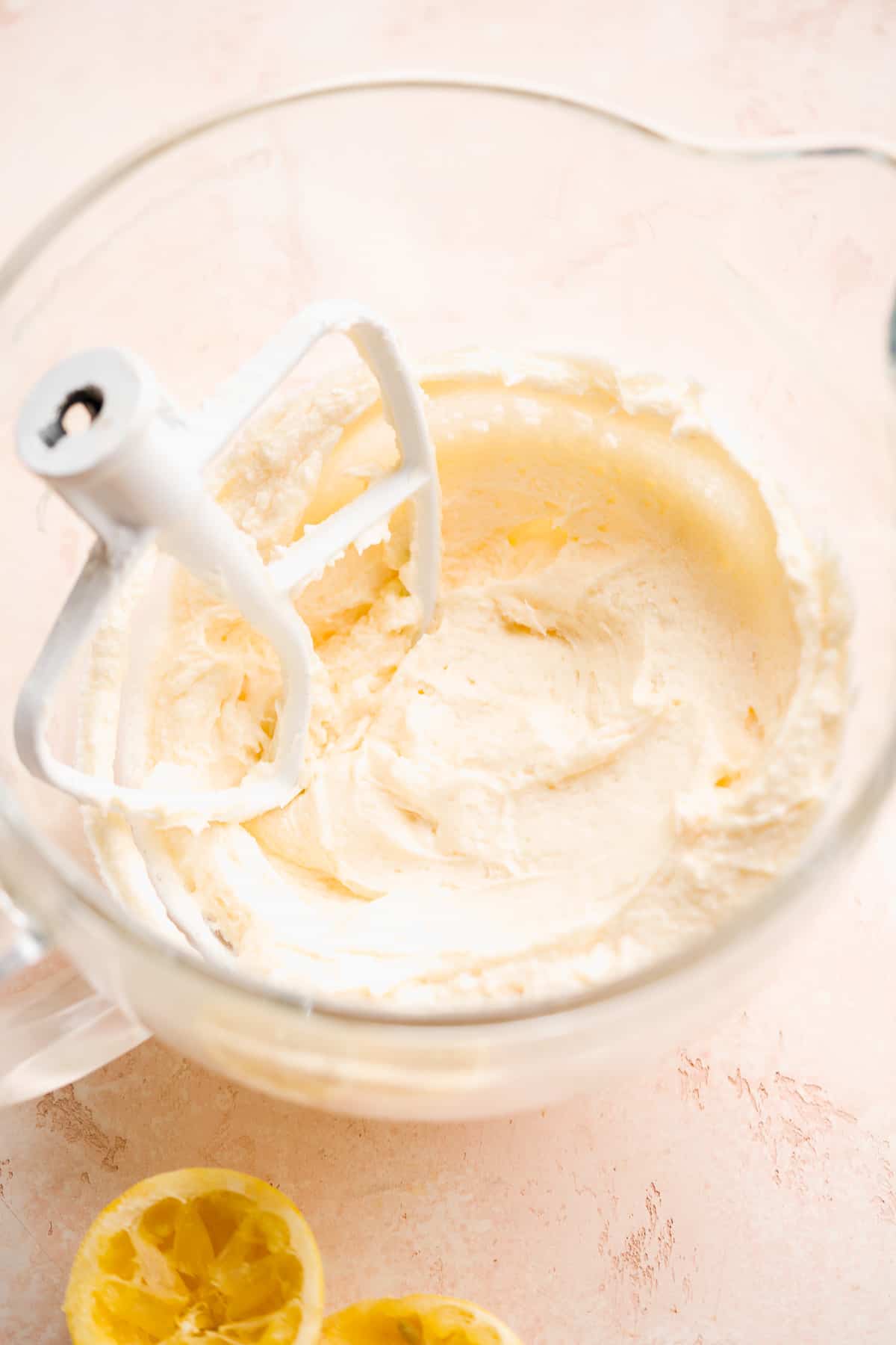 Glass bowl with white icing and a whisk resting inside.