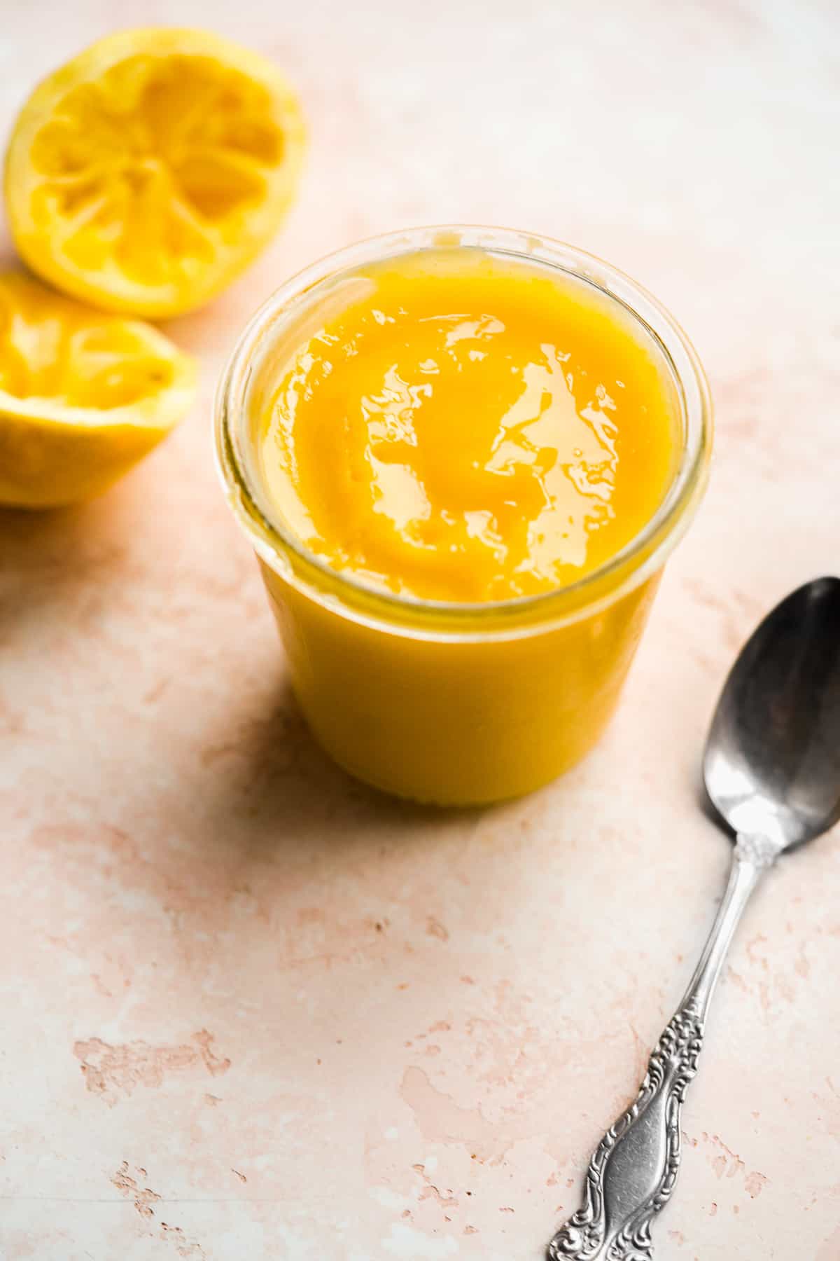 Glass jar of lemon curd with a spoon on the ground.
