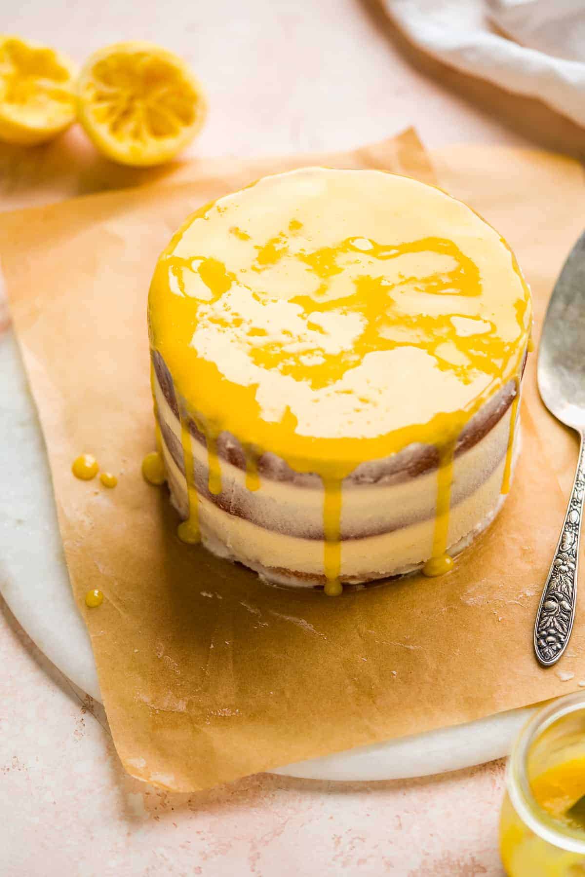 Round cake with lemon drizzle on top on brown parchment paper.