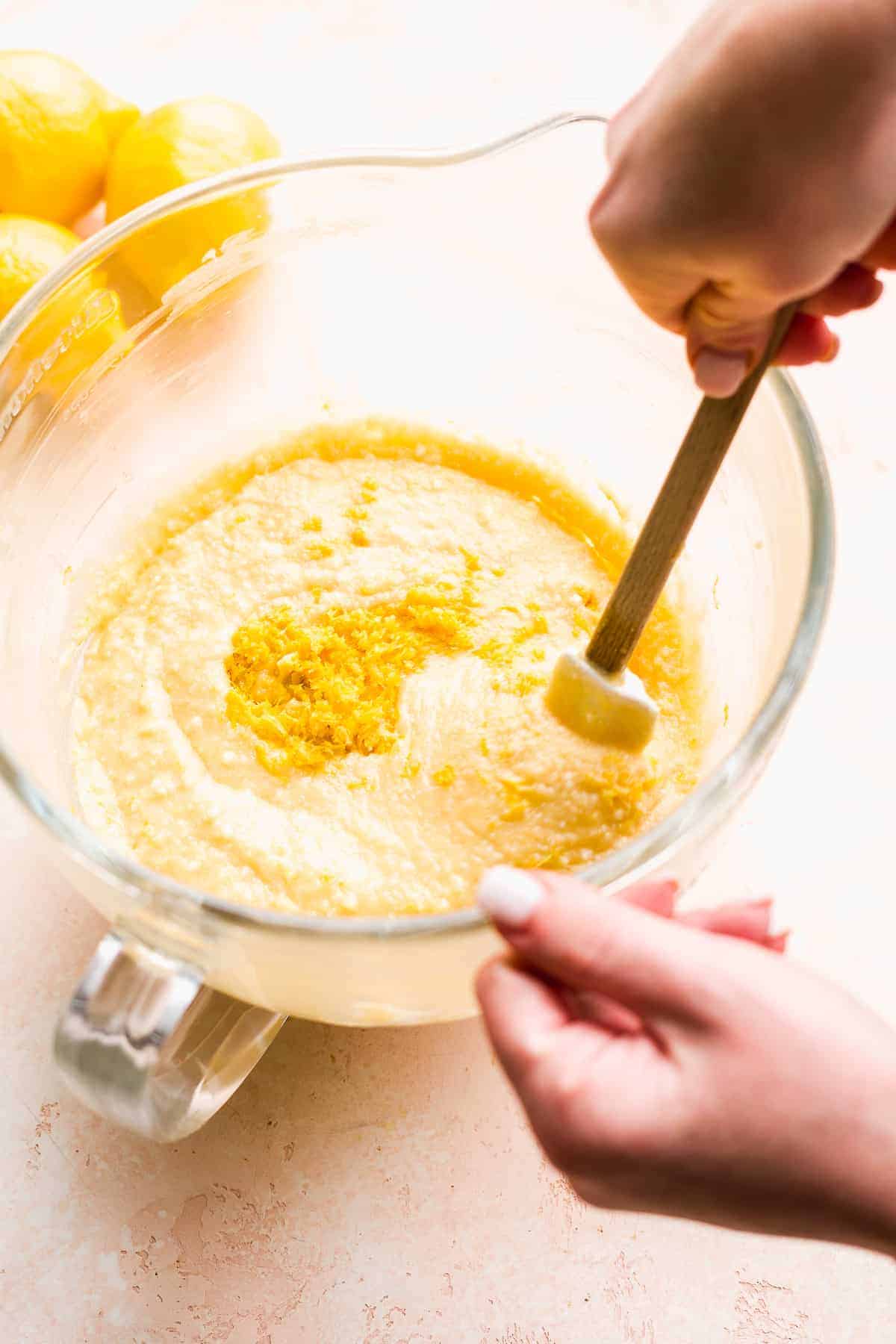 Hand folding lemon zest into cake batter with rubber spatula.