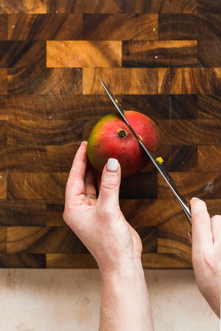 Person slicing mango on a wooden cutting board.