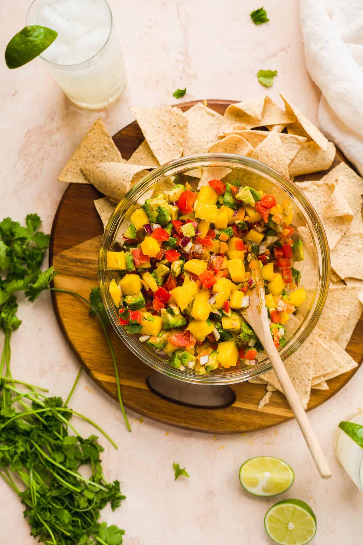 Bowl of chunky mango salsa with avocados with chips and cilantro on the side.