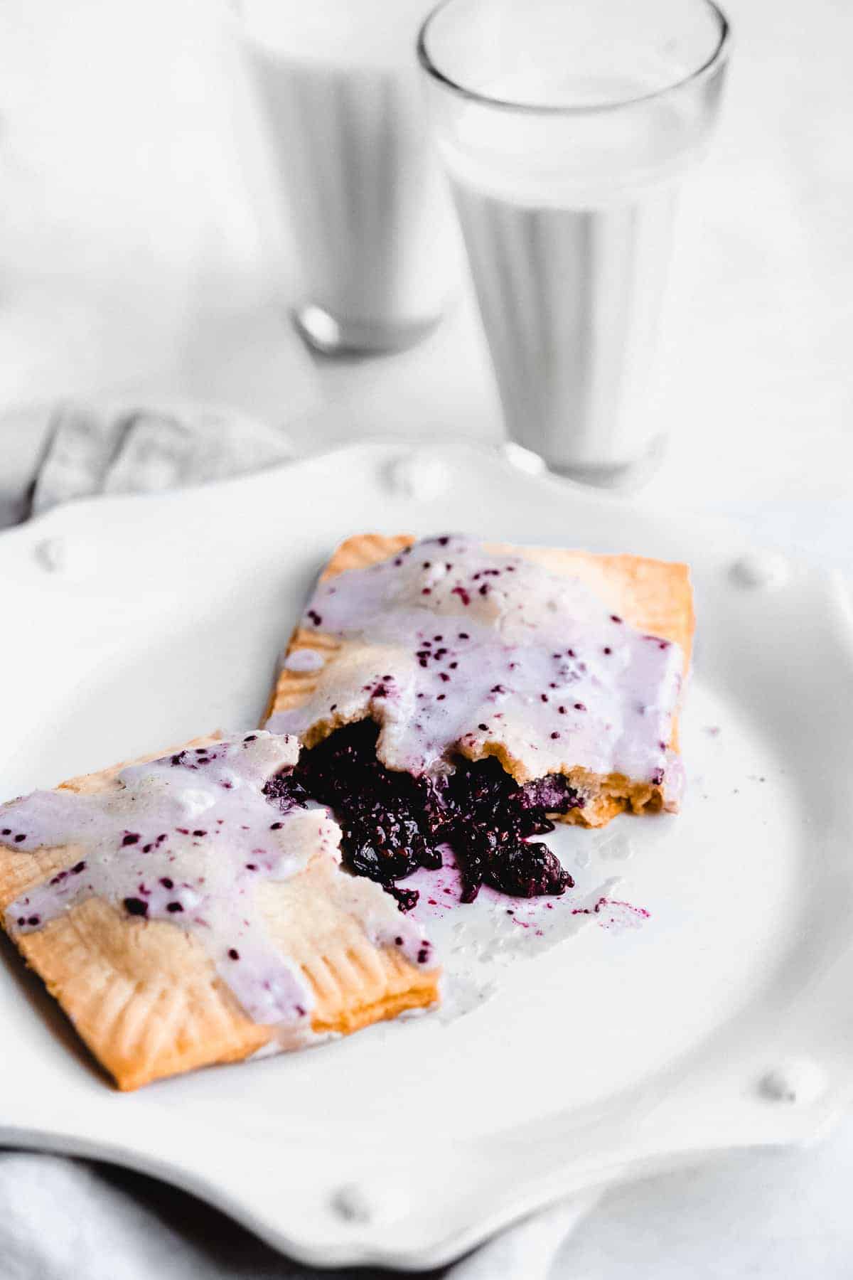 Pop tart broken open on a plate with blueberry jam spilling out and frosting.