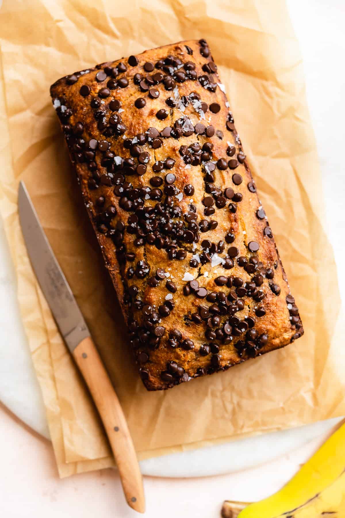 Chocolate chip bread sitting on brown paper with a knife to the side.