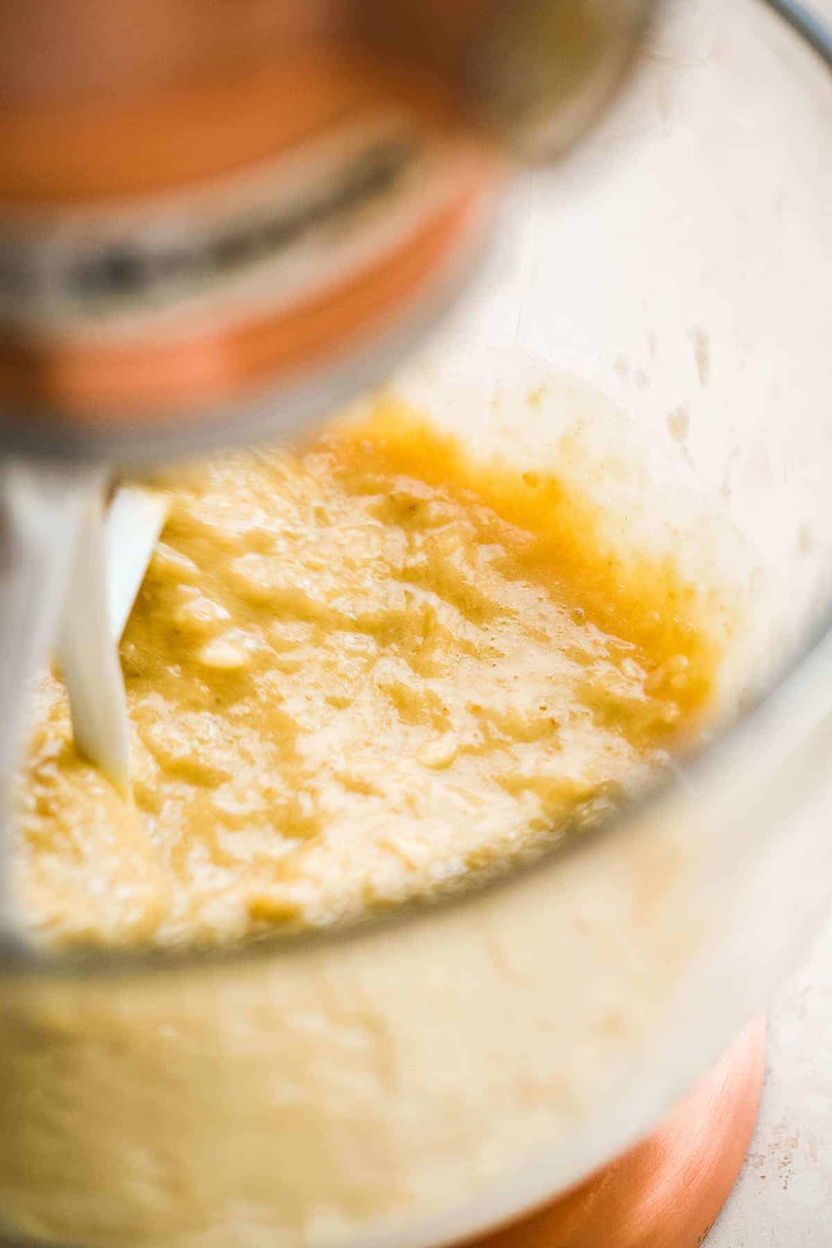 Glass bowl with tan mixture and a beater mixing everything together.