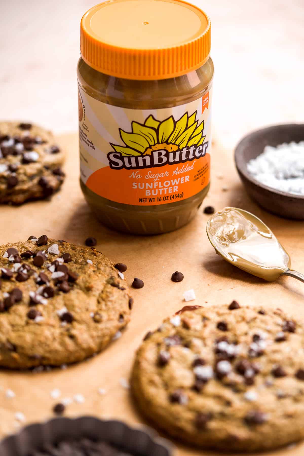 Jar of sunflower butter with orange lid on parchment paper with cookies on the surface.