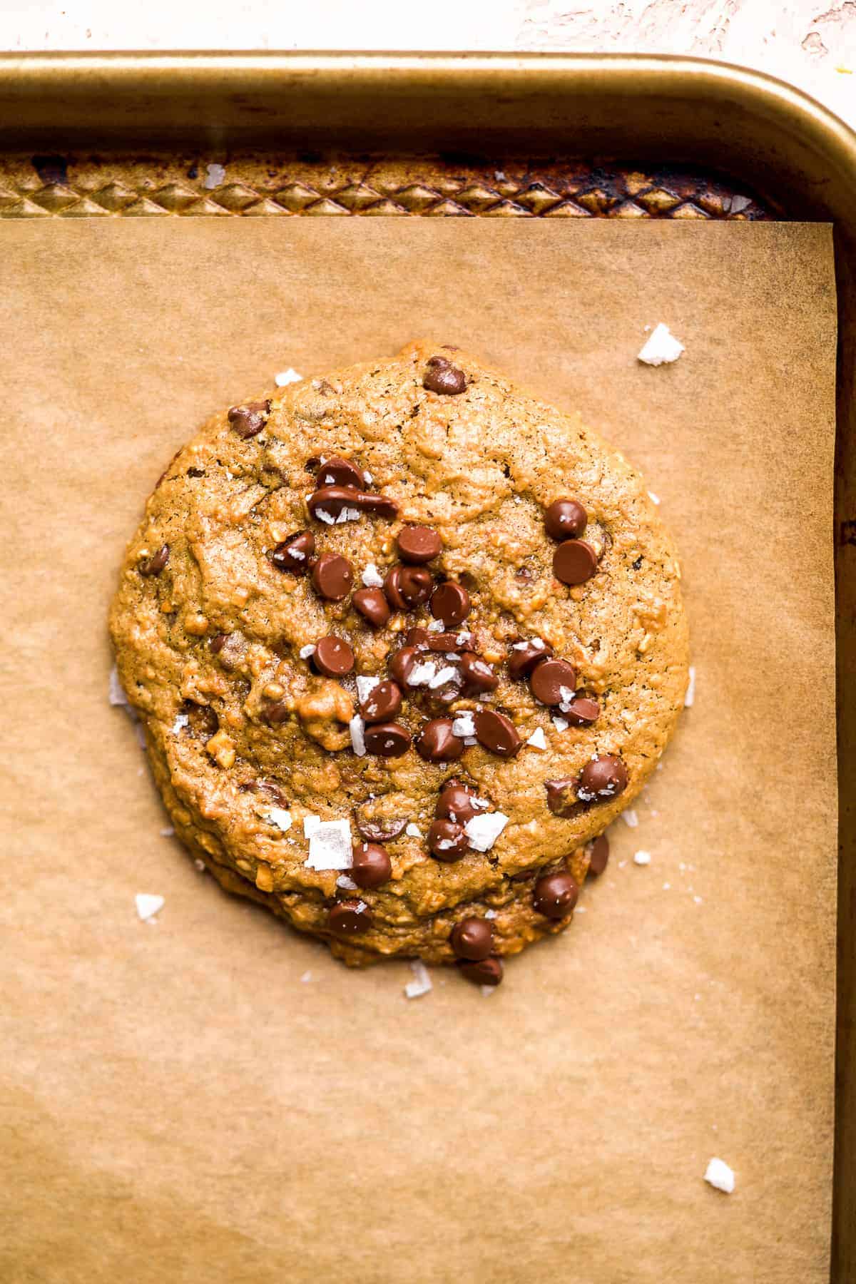 Chocolate chip cookie on a baking pan with parchment paper and sea salt on top.