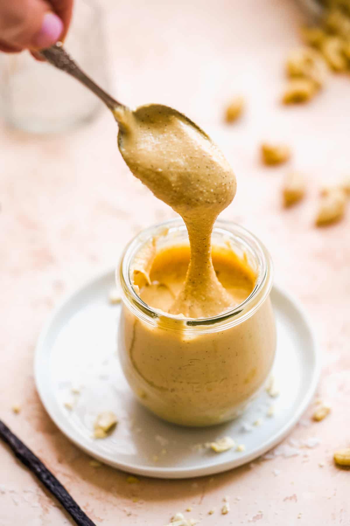 Hand dipping spoon in jar of cashew butter.