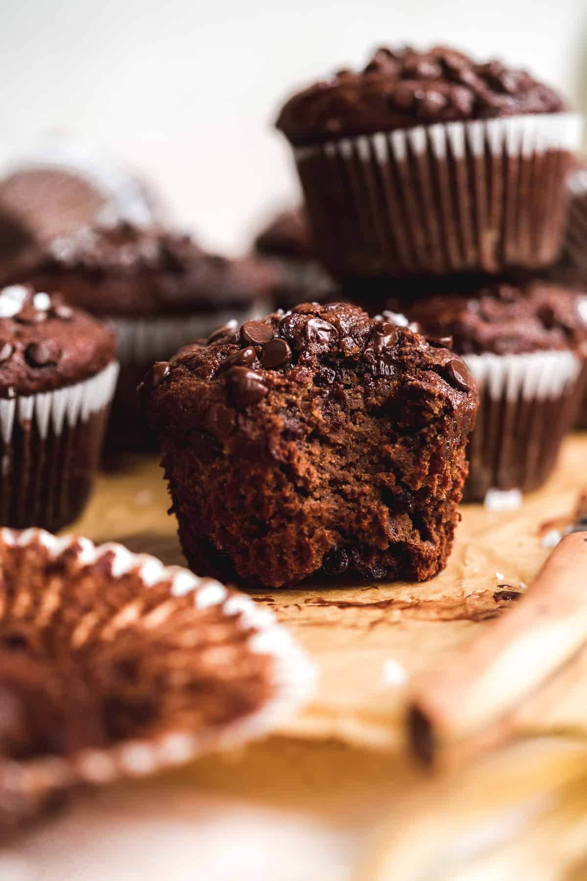 Up close view of chocolate muffin with a bite taken out of it on brown parchment paper.