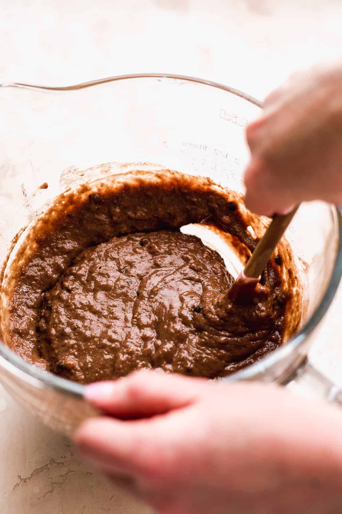 Hand mixing a chocolate batter in a glass bowl.