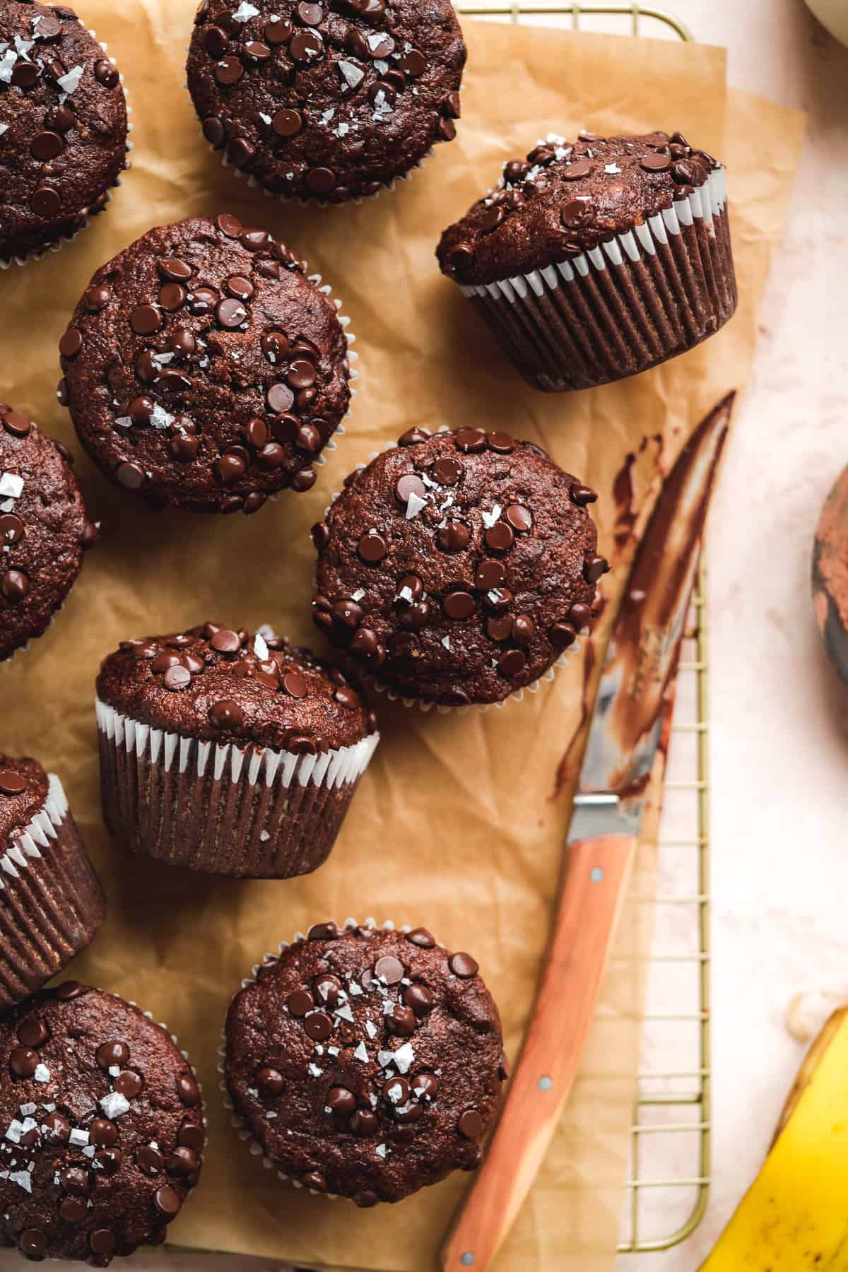Chocolate muffins with liners scattered on brown paper.