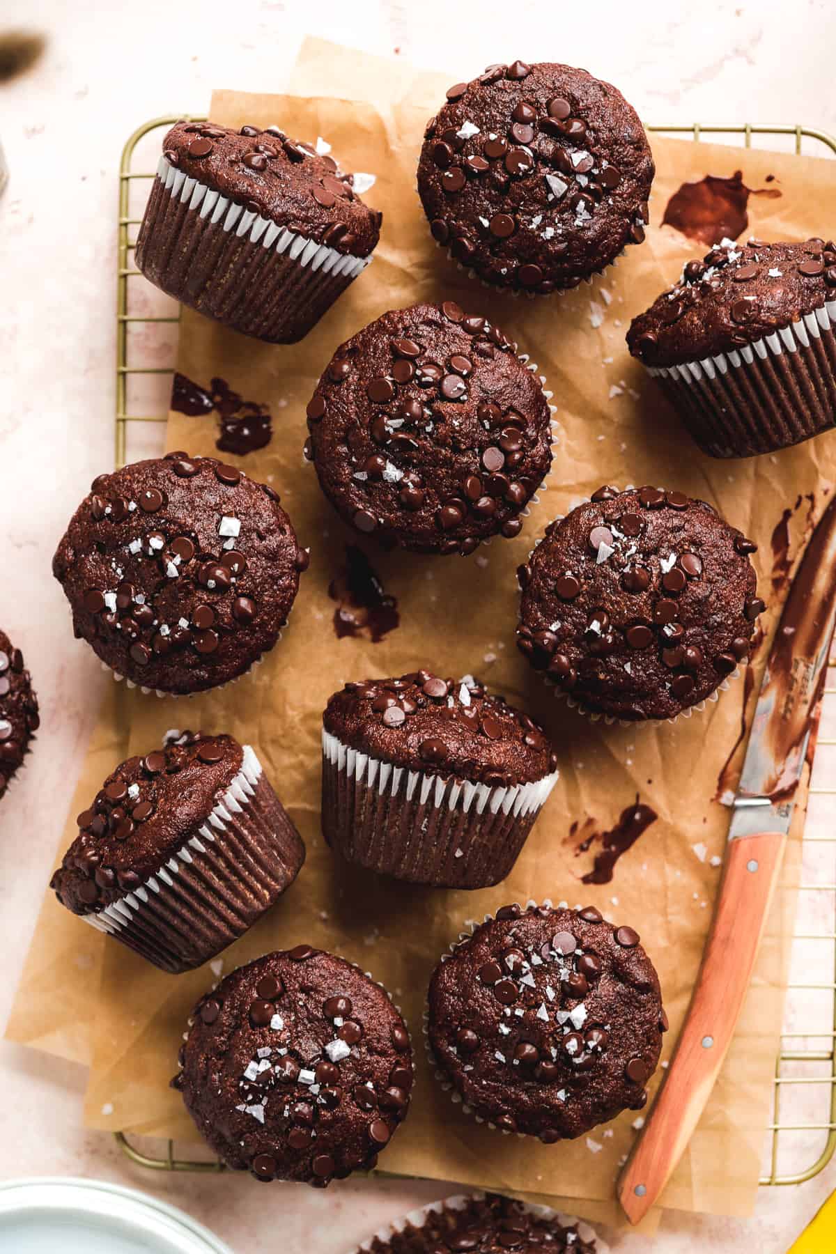 Chocolate muffins scattered on a cooling rack with parchment paper.