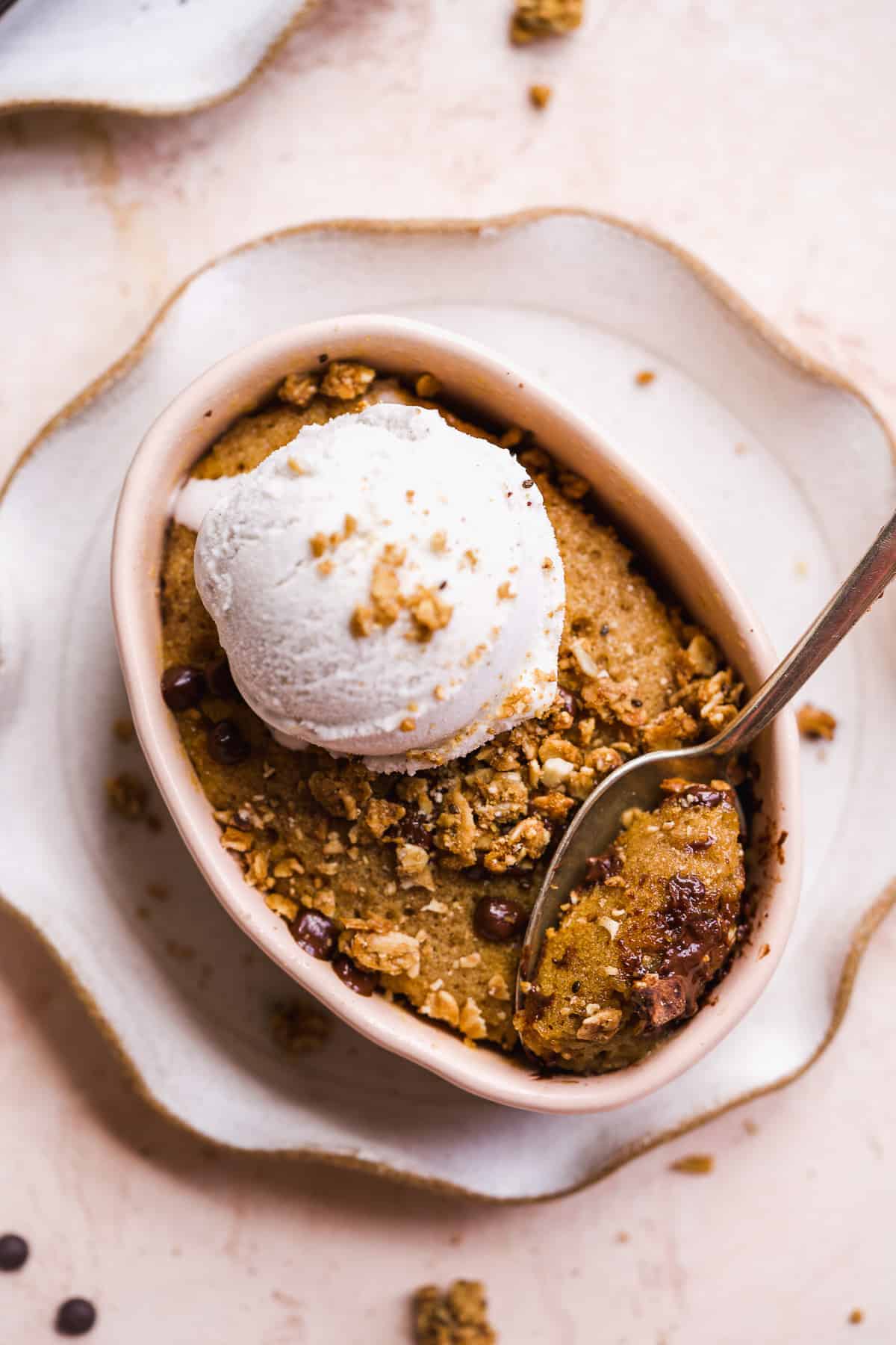 Oval dish with chocolate chip cookie baked inside and ice cream scoop on top.