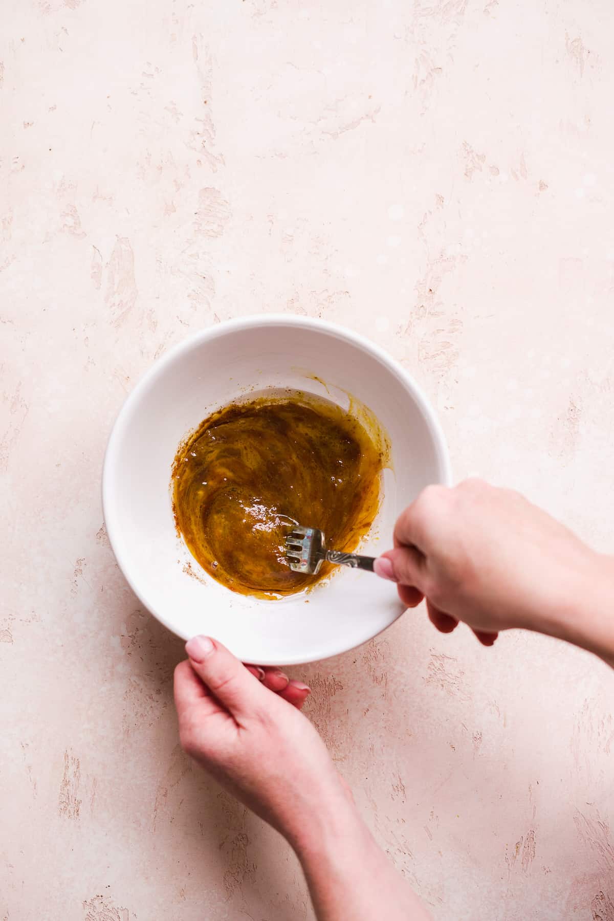 Person whisking wet ingredients in a white bowl.