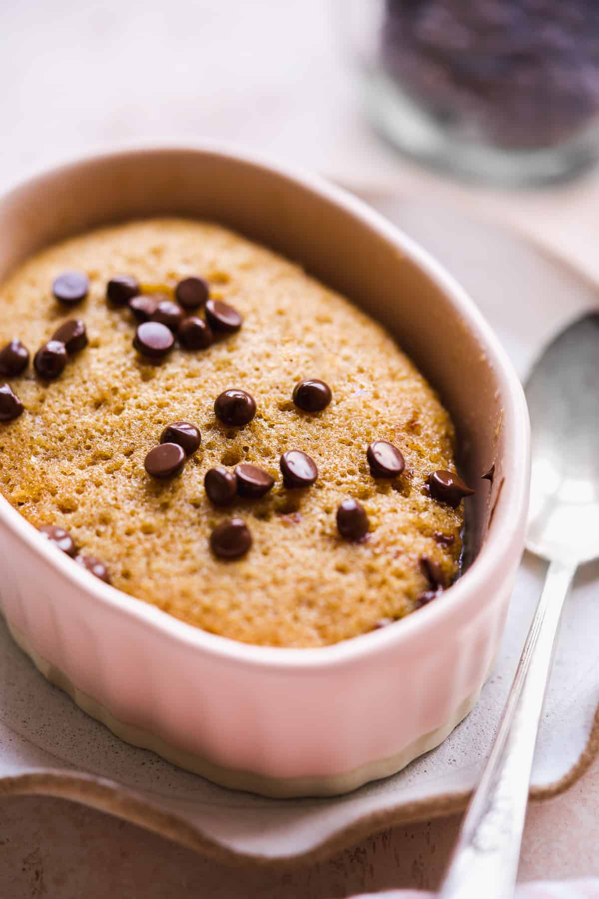 Side view of a cake baked in a small ramekin with chocolate chips on top.