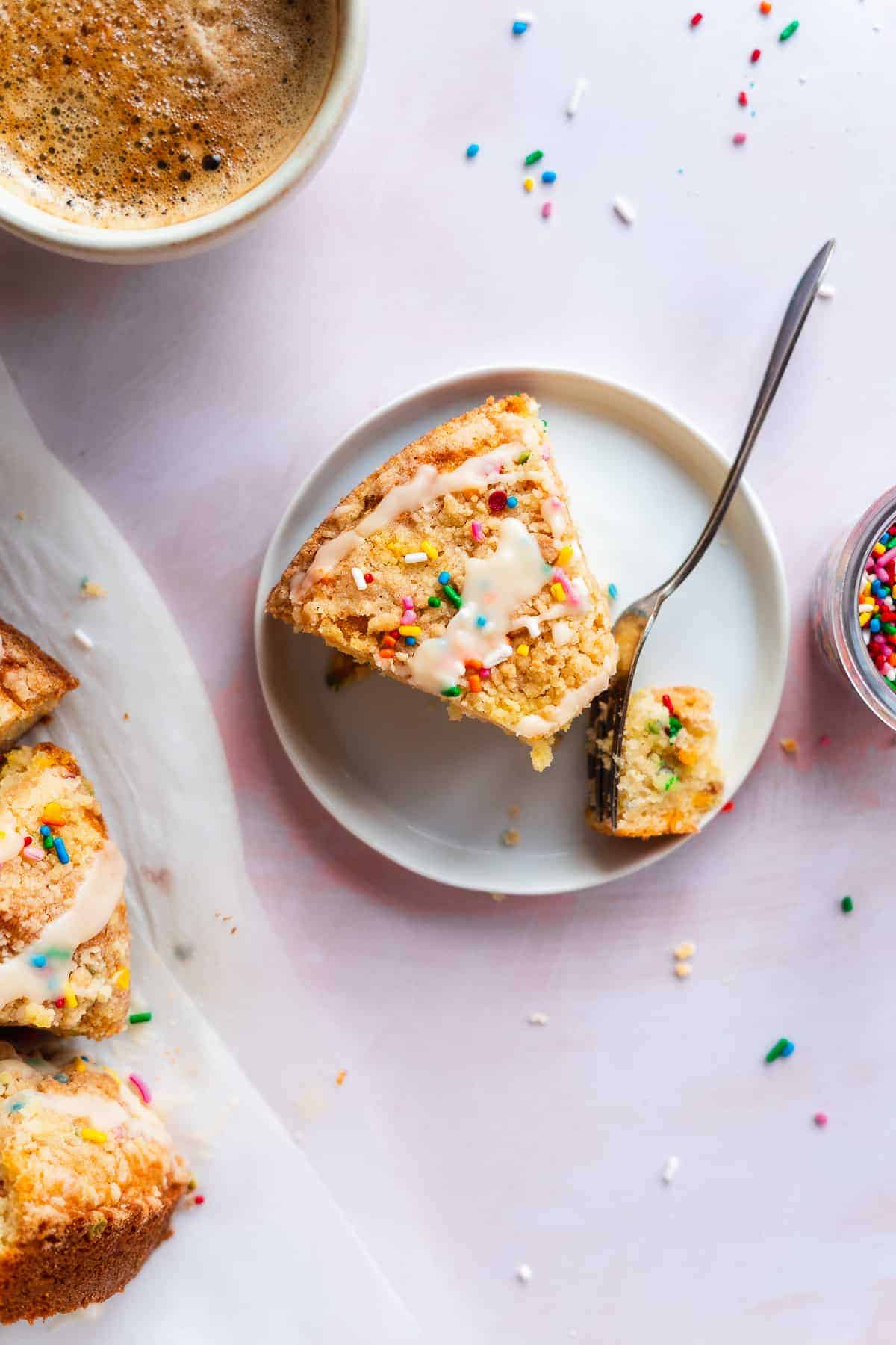 Slice of coffee cake with sprinkles on a small white plate with a fork.