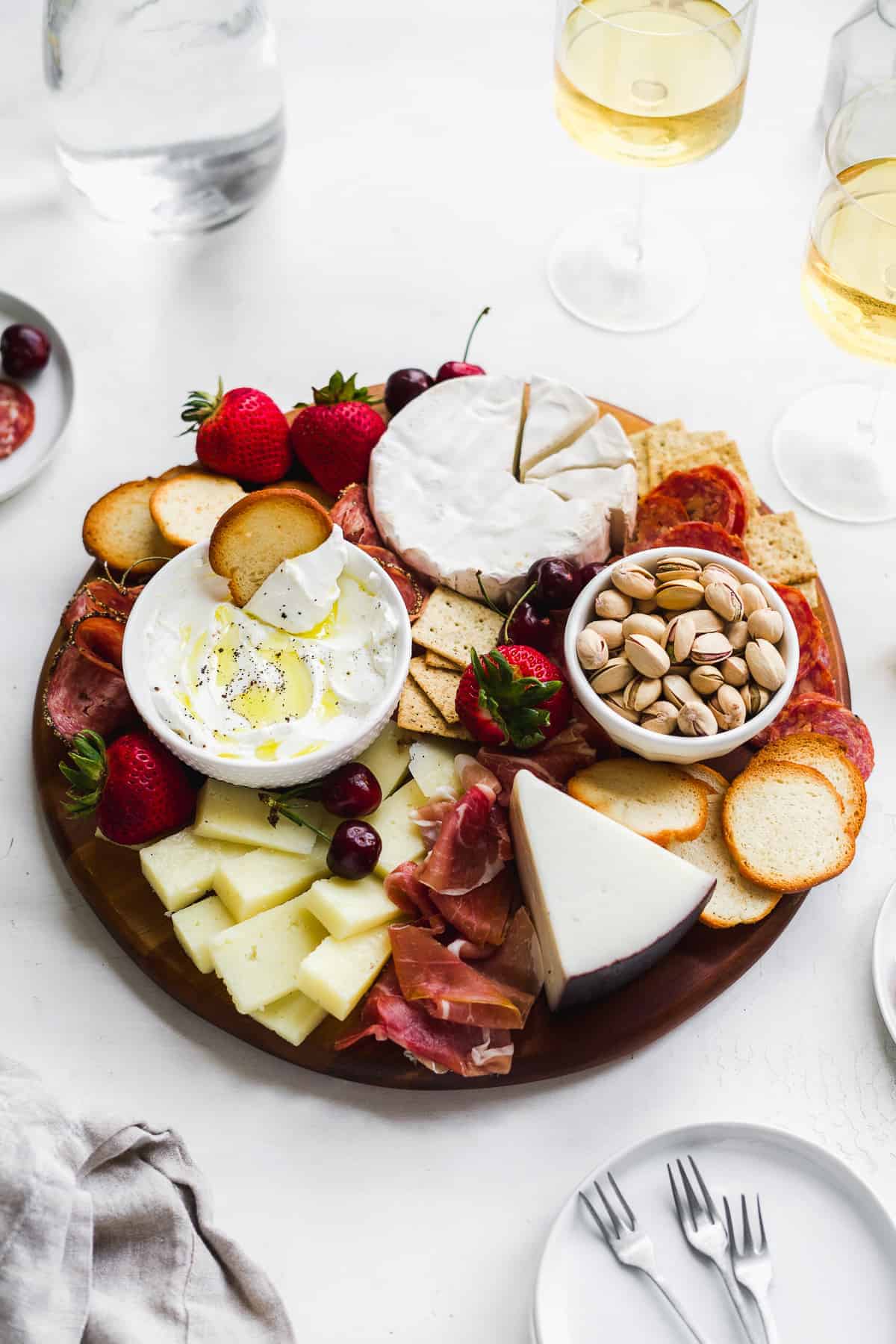 Wooden board filled with meats and cheeses and wine on the side.