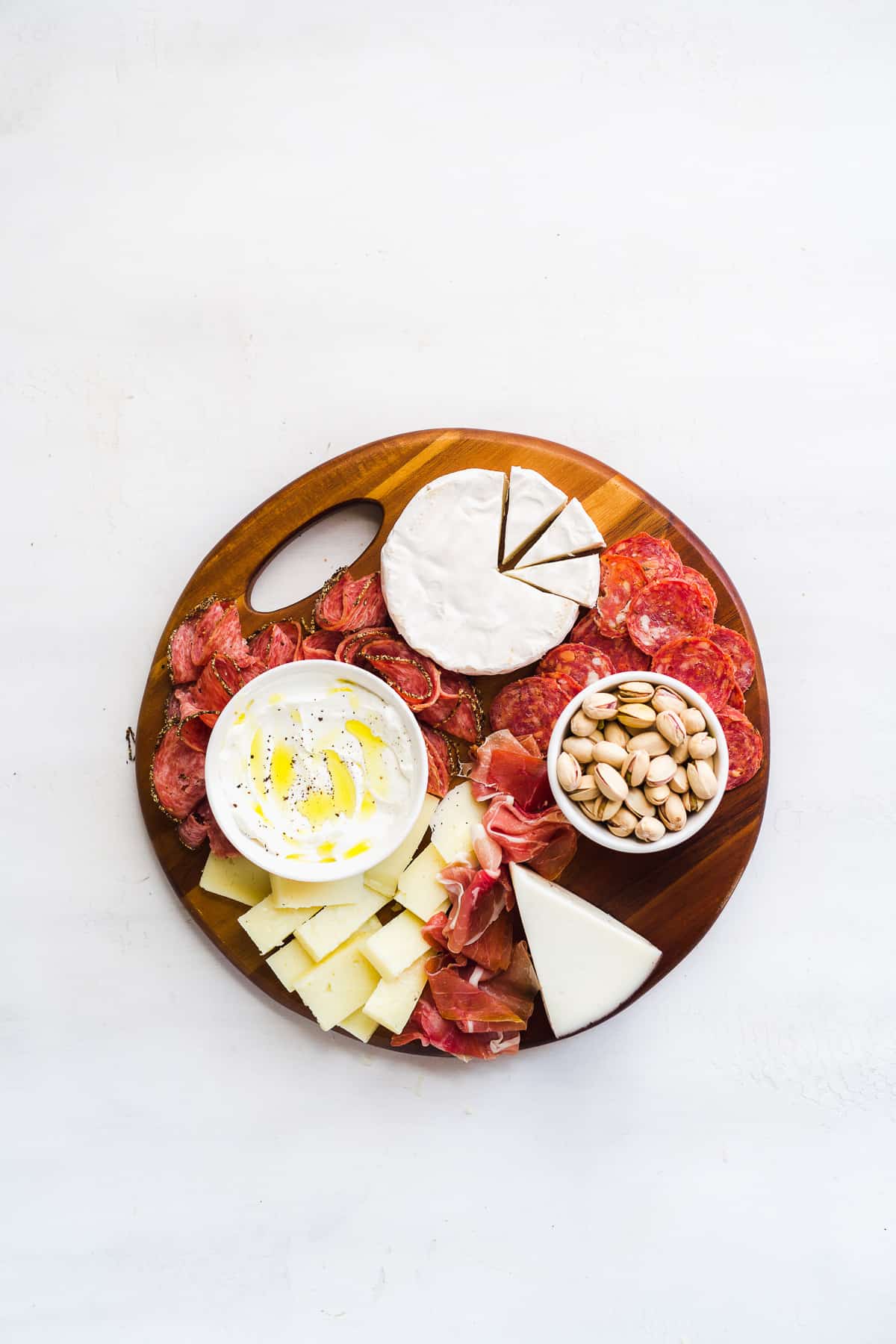 Platter with cheeses and meats on a white surface.