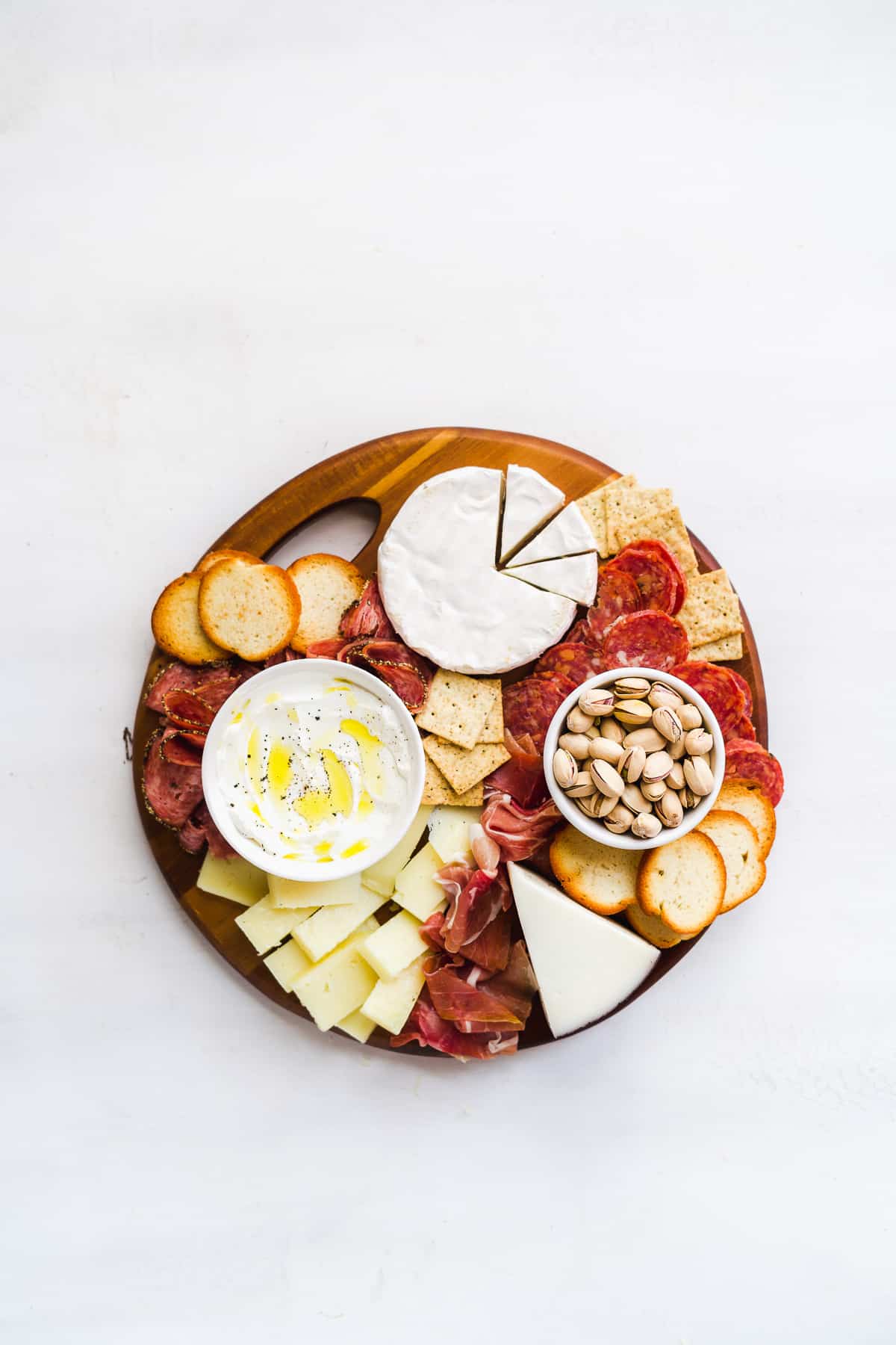 Wooden platter with meats and cheeses on a white surface.