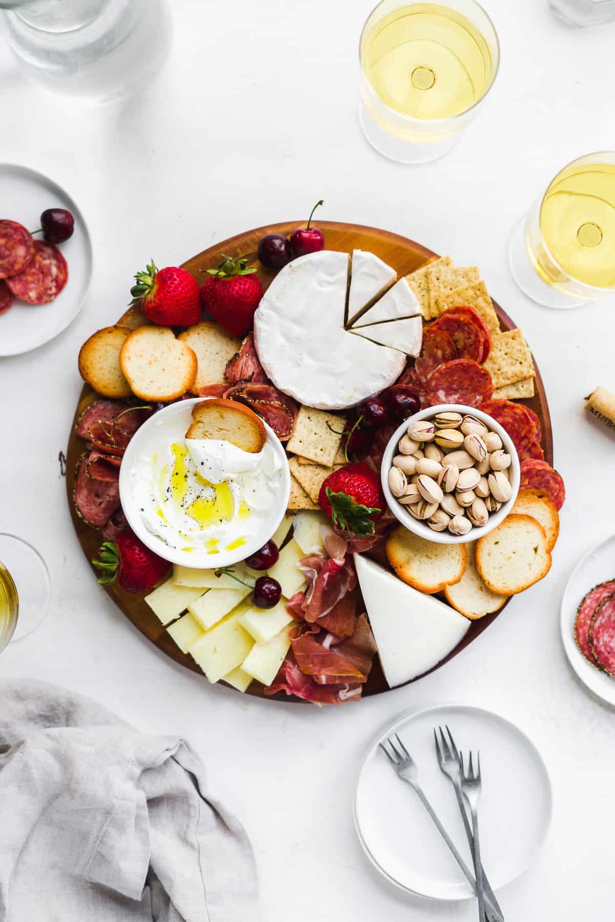 Charcuterie board with cheeses and fruit and wine on the side.