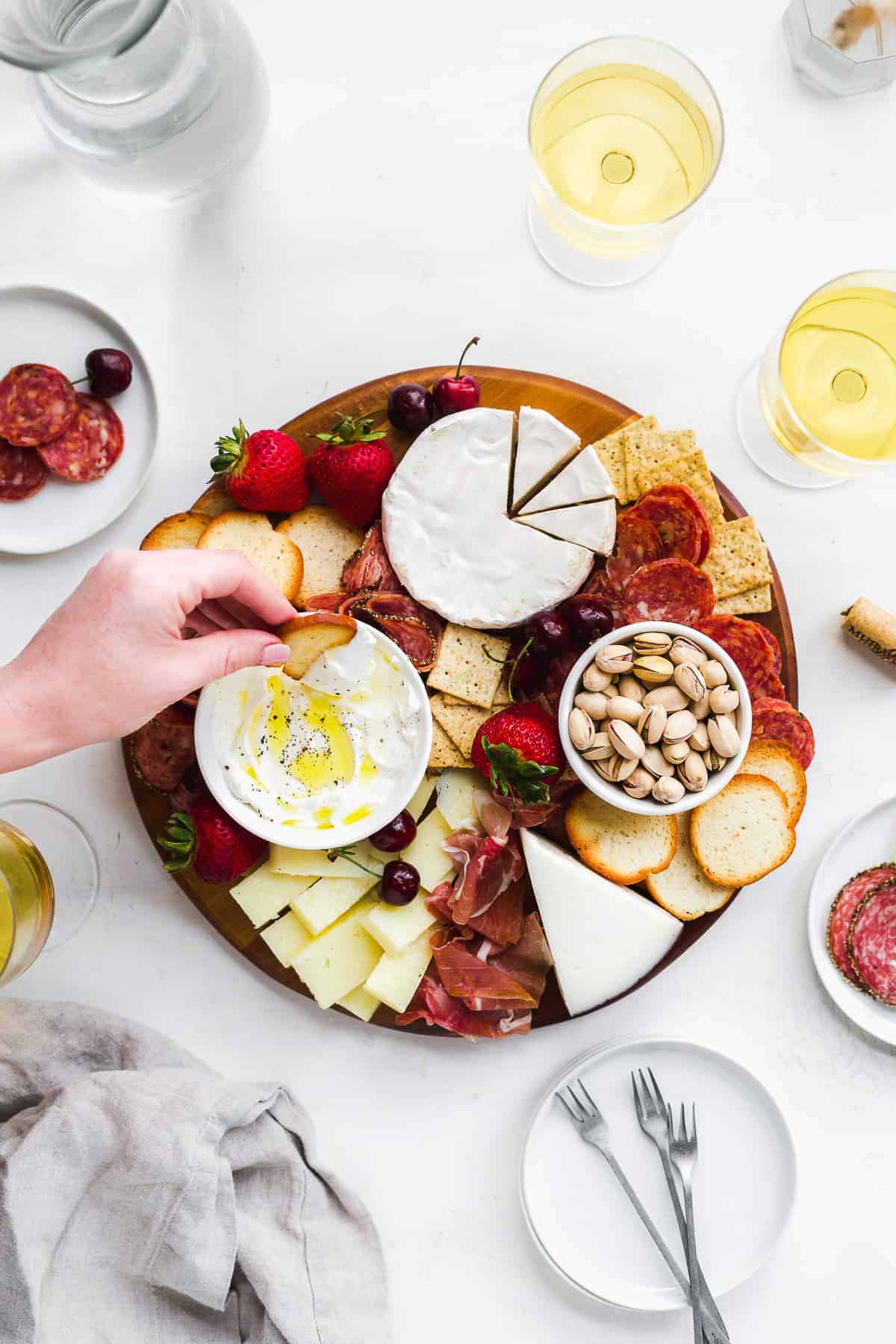 Hand dipping cracker in a bowl on a charcuterie board with meats and cheeses.