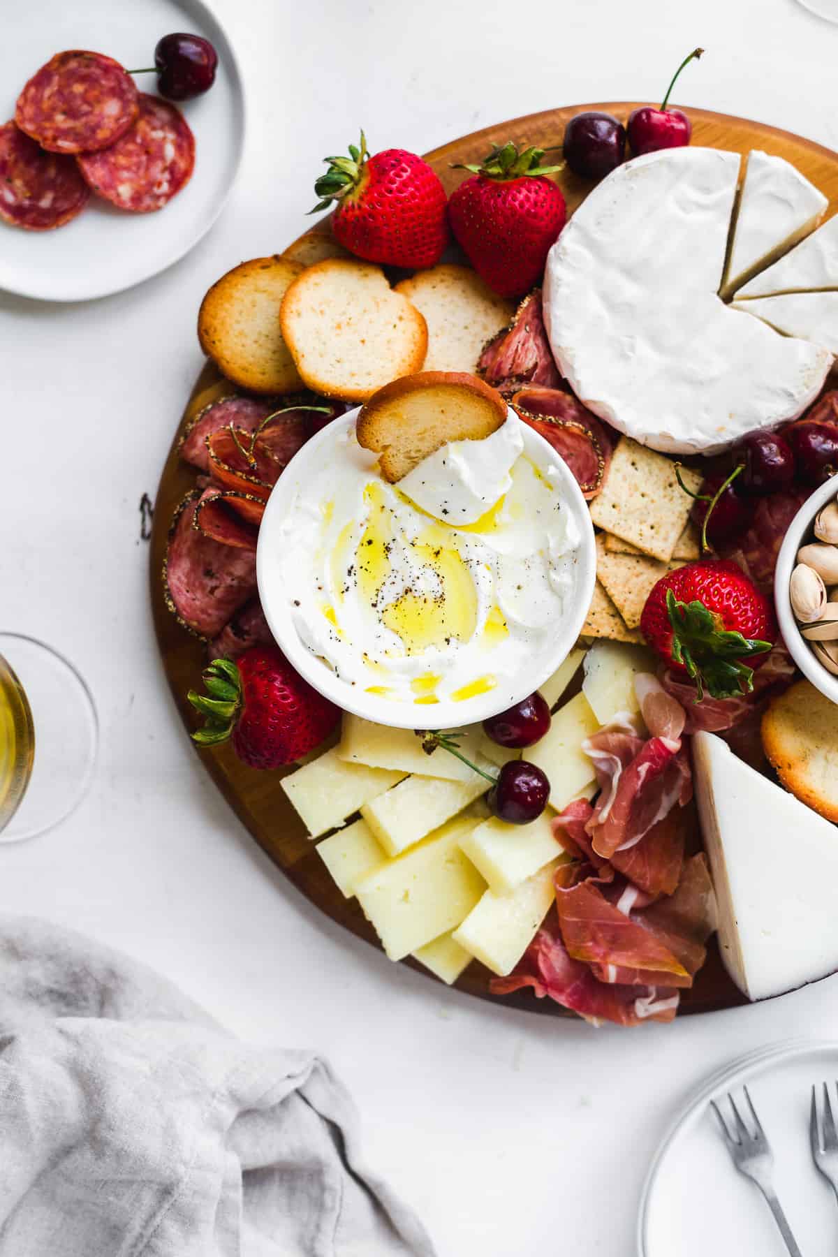 Circular platter with meat and cheeses and glass of wine on the side.