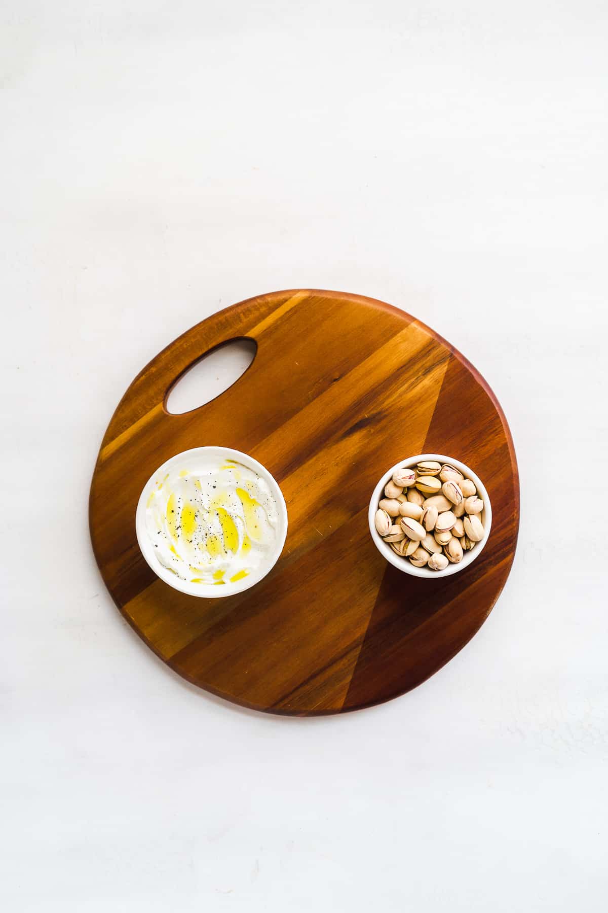 Wooden circular platter with two bowls on it on a white surface.