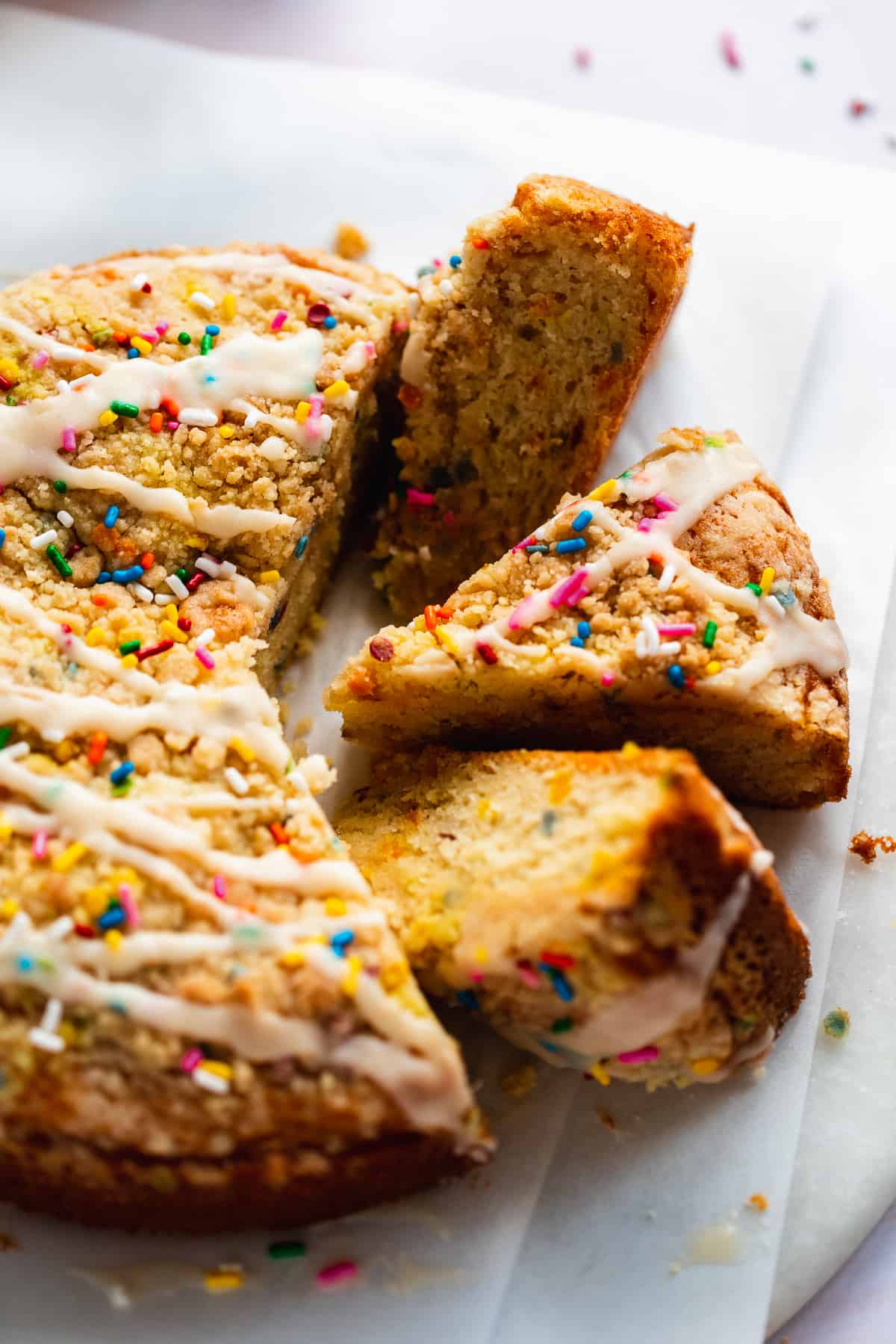 Coffee cake with sprinkles and icing on top cut into triangles.