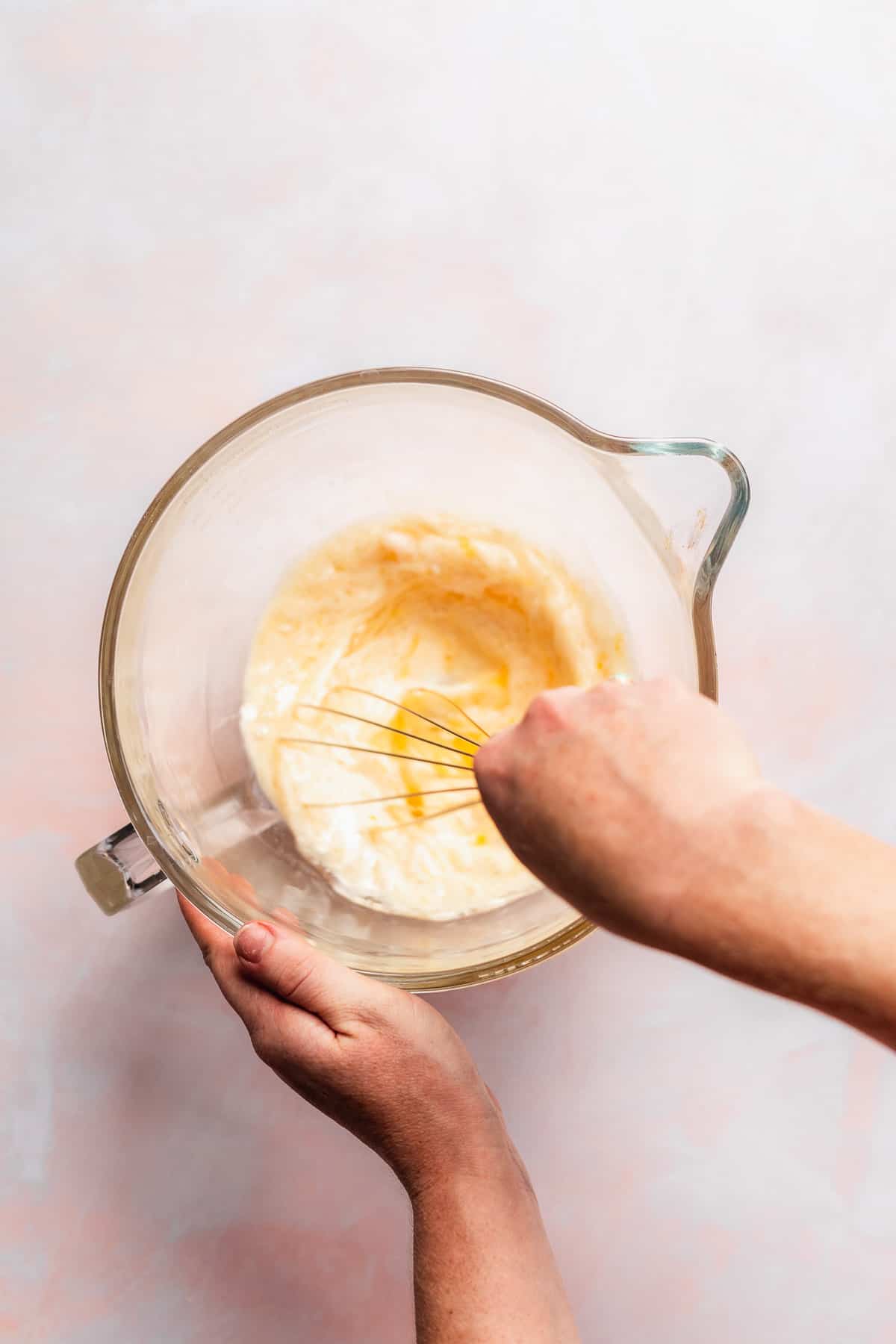Person whisking a mixture in a glass mixing bowl.