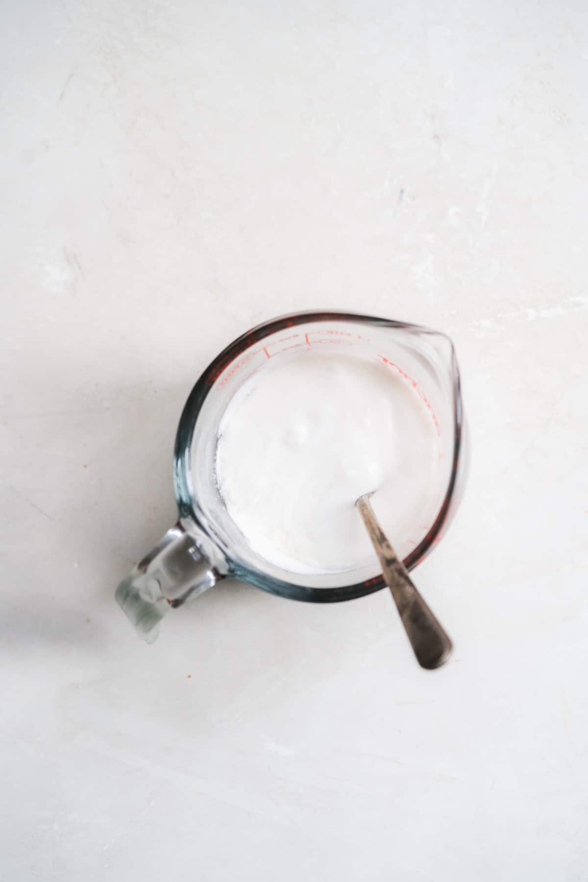 Overhead view of coconut milk in a measuring cup with a spoon.