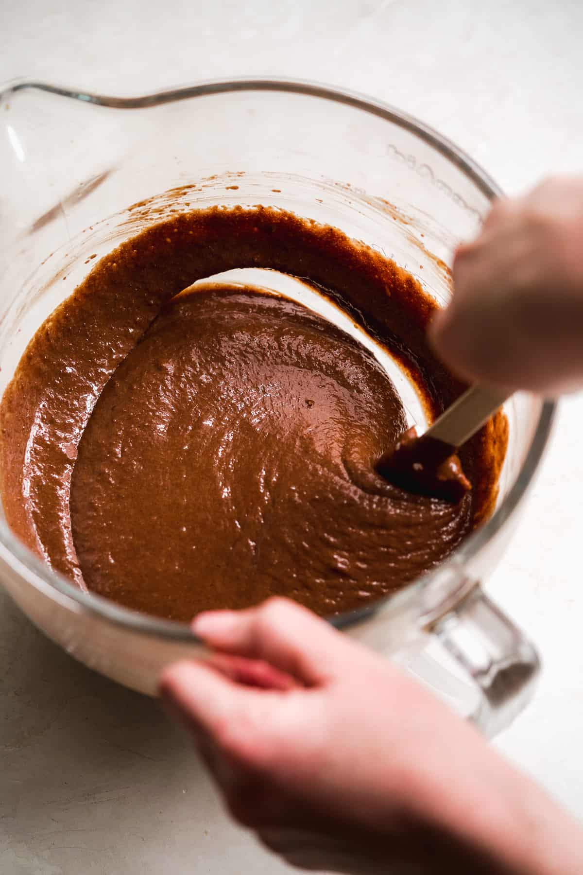 Hand mixing chocolate batter in a glass bowl with a rubber spatula.