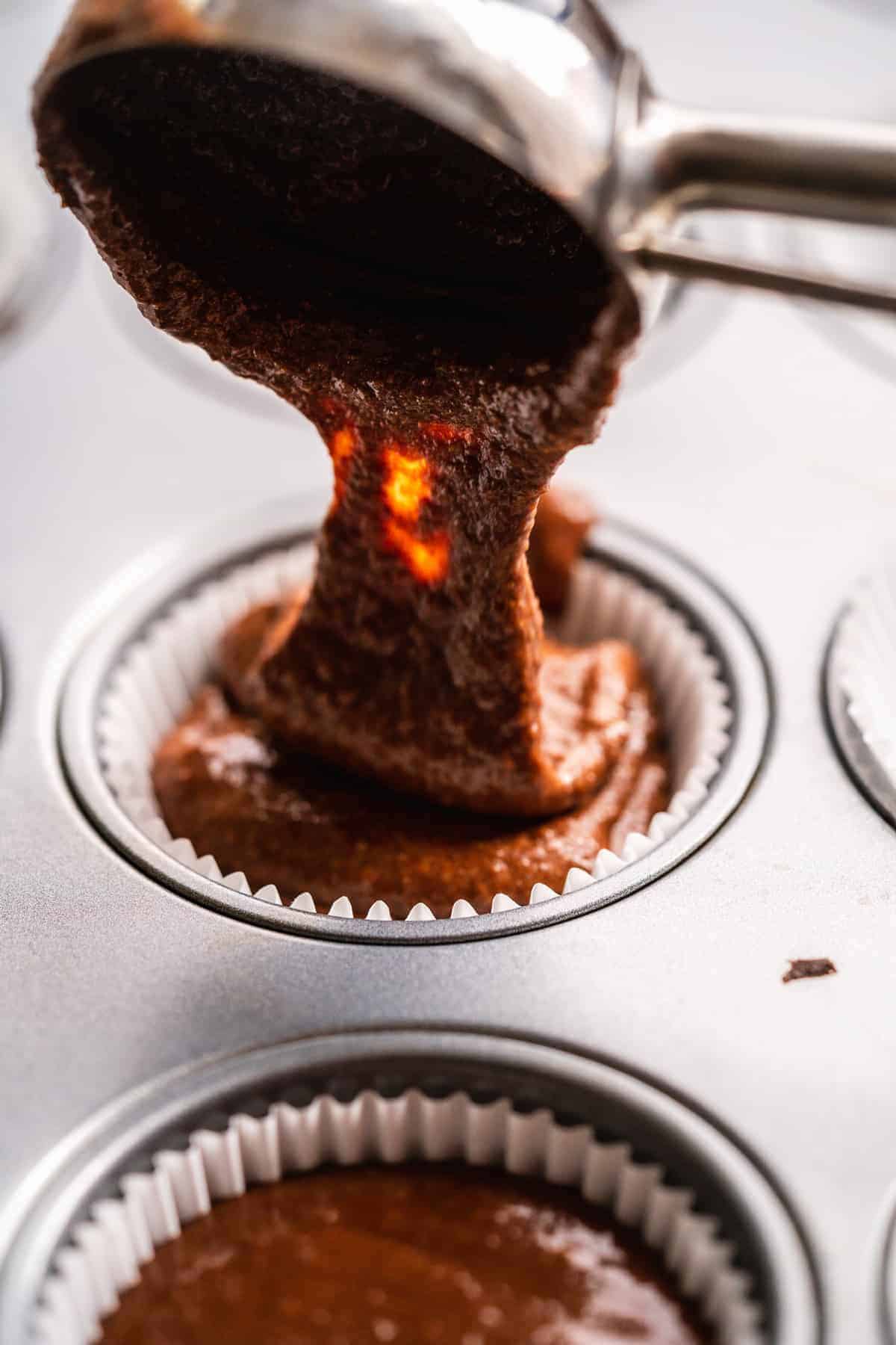 Cookie scoop pouring chocolate batter into cupcake liners.