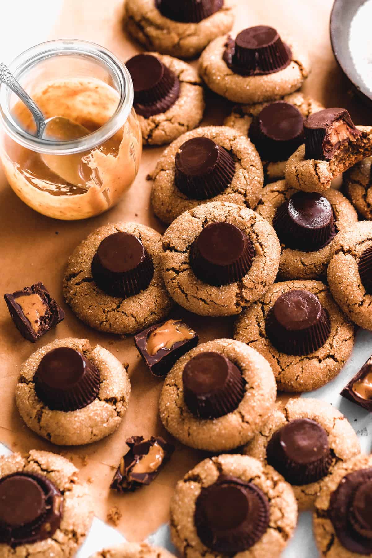 Peanut butter cookies with a peanut butter cup on top scattered on brown parchment paper.