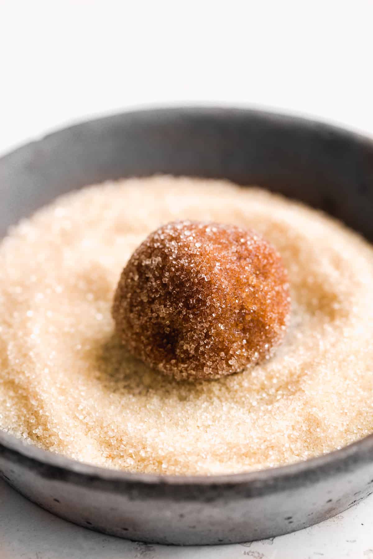 Ball of cookie dough rolled in a dish with corse sugar.