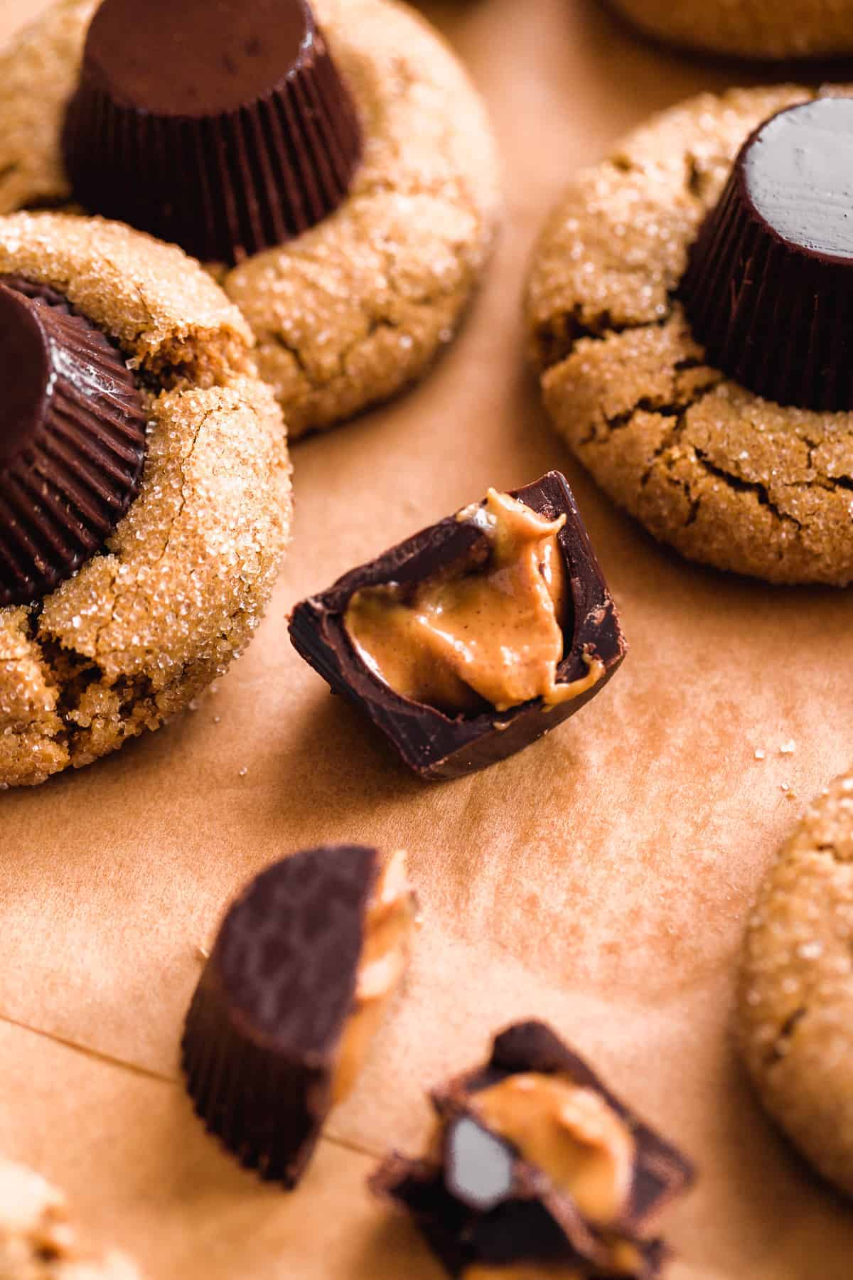 Mini peanut butter cup cut in half on brown paper with cookies around it.