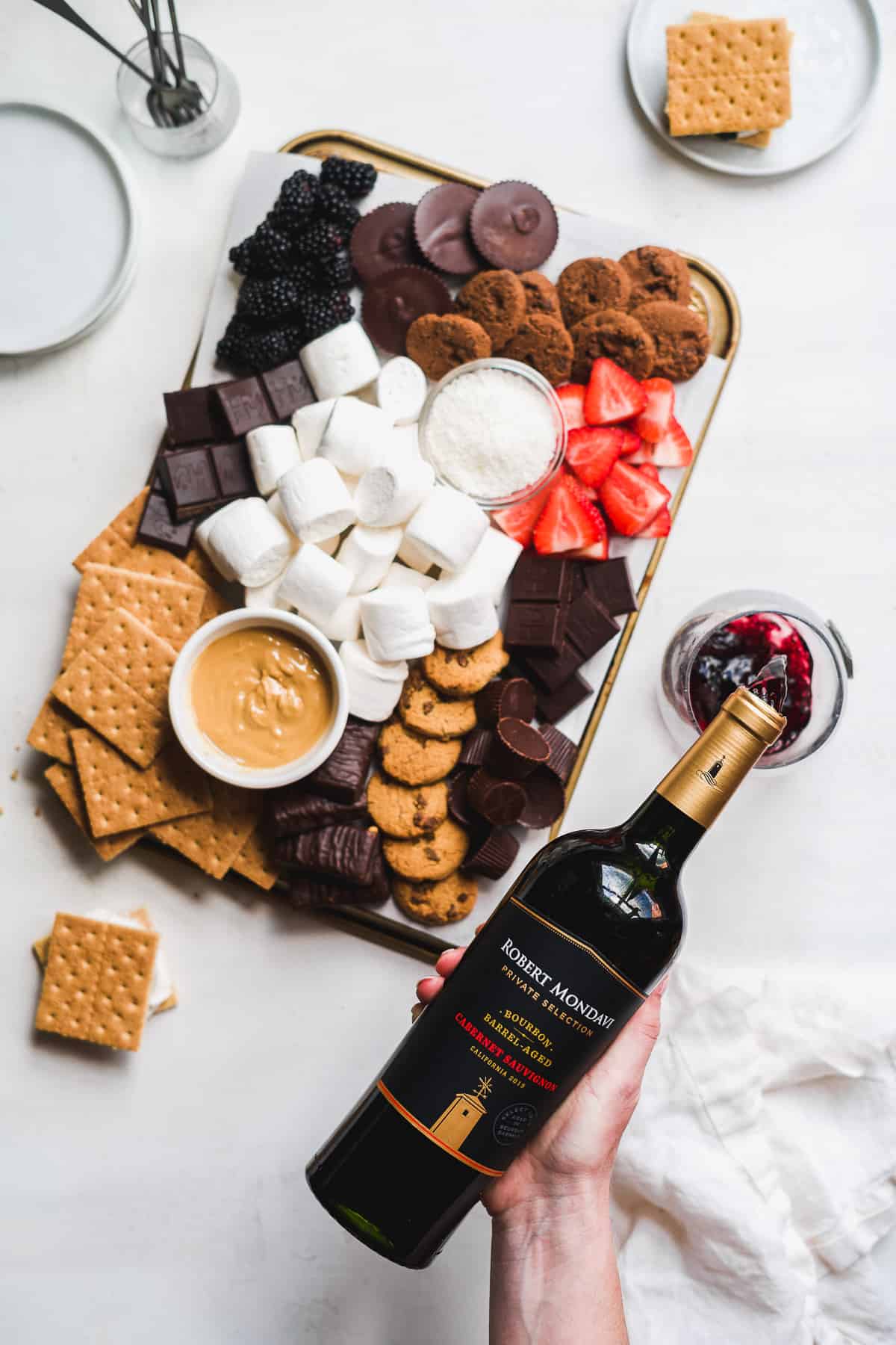 Hand pouring red wine into wine glass with a dessert board to the side.
