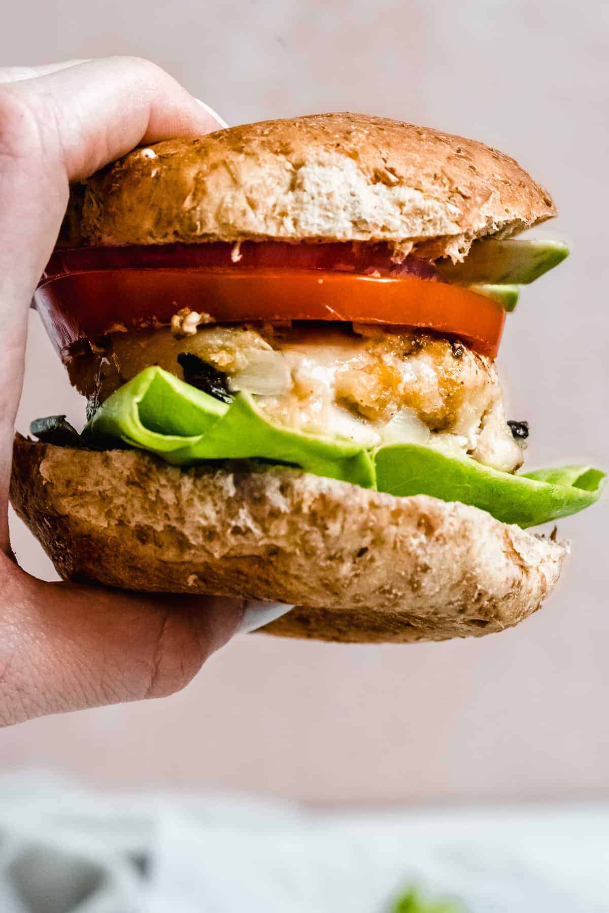 Hand holding burger with lettuce and tomato and bun on top.