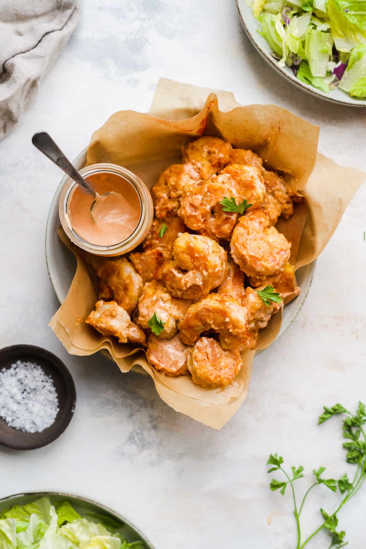 Bang bang shrimp in a basket with parchment paper and sauce on the side.