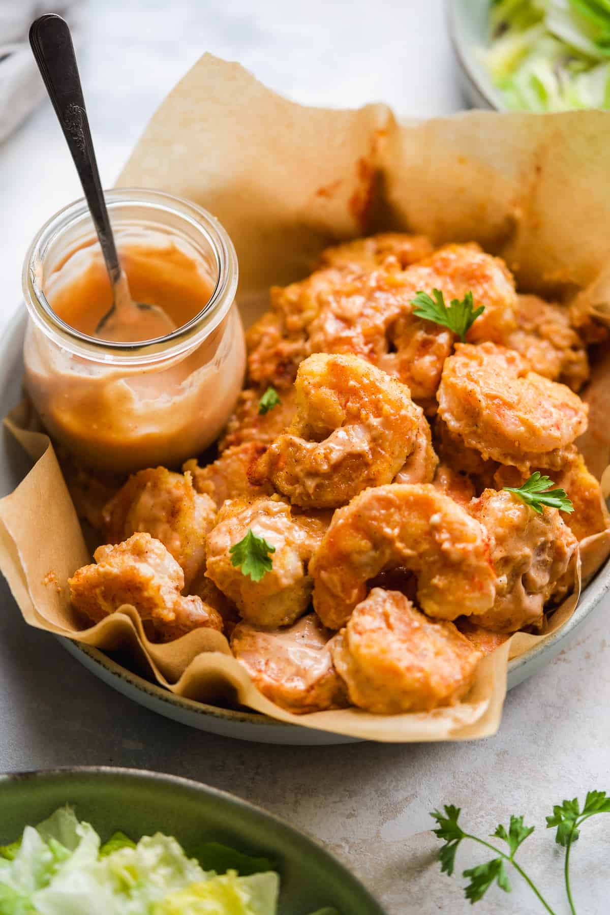 Orange shrimp tossed in sauce in a basket with brown paper.
